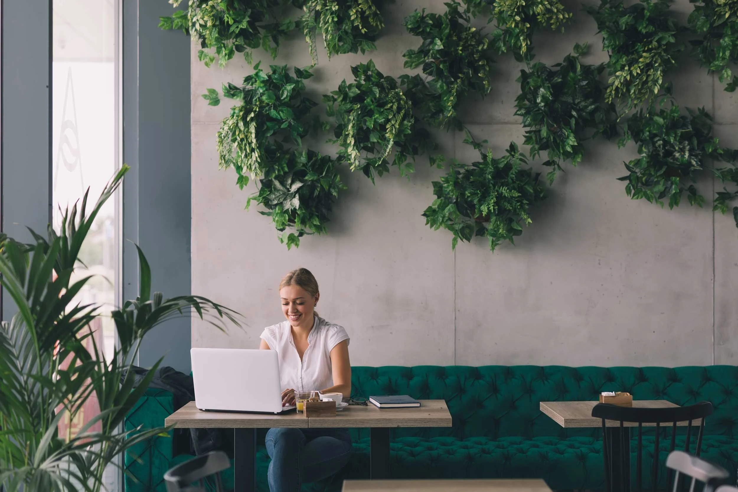 Woman working at her laptop in a plant decorated with a plush jewel sofa and lots of foliage