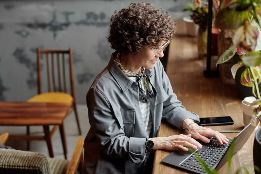 Curly hair mature woman working at her laptop on a wooden desk laden with beautiful potted plants