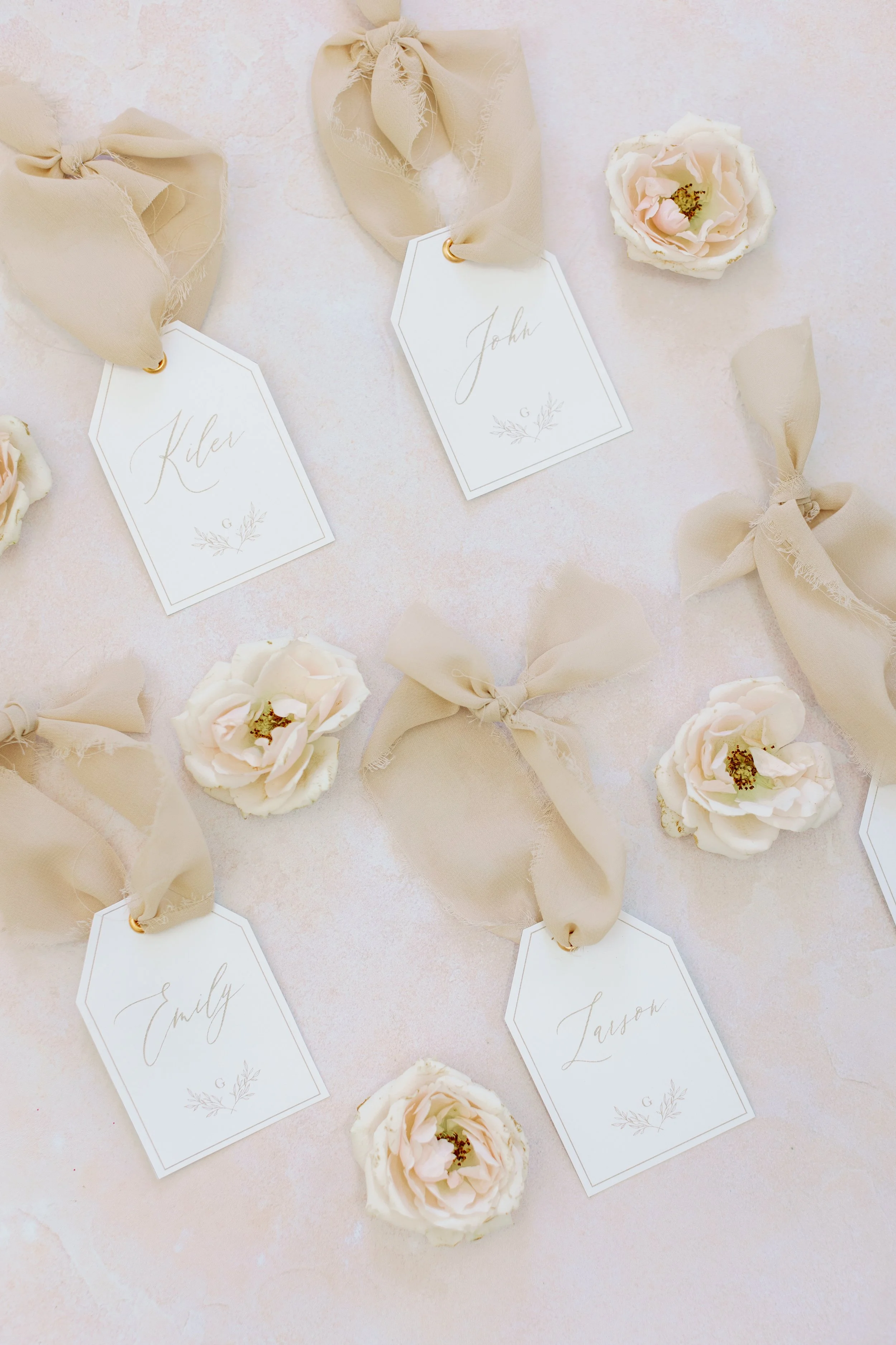 Elegant name tags with beige ribbons and white roses on a light background.