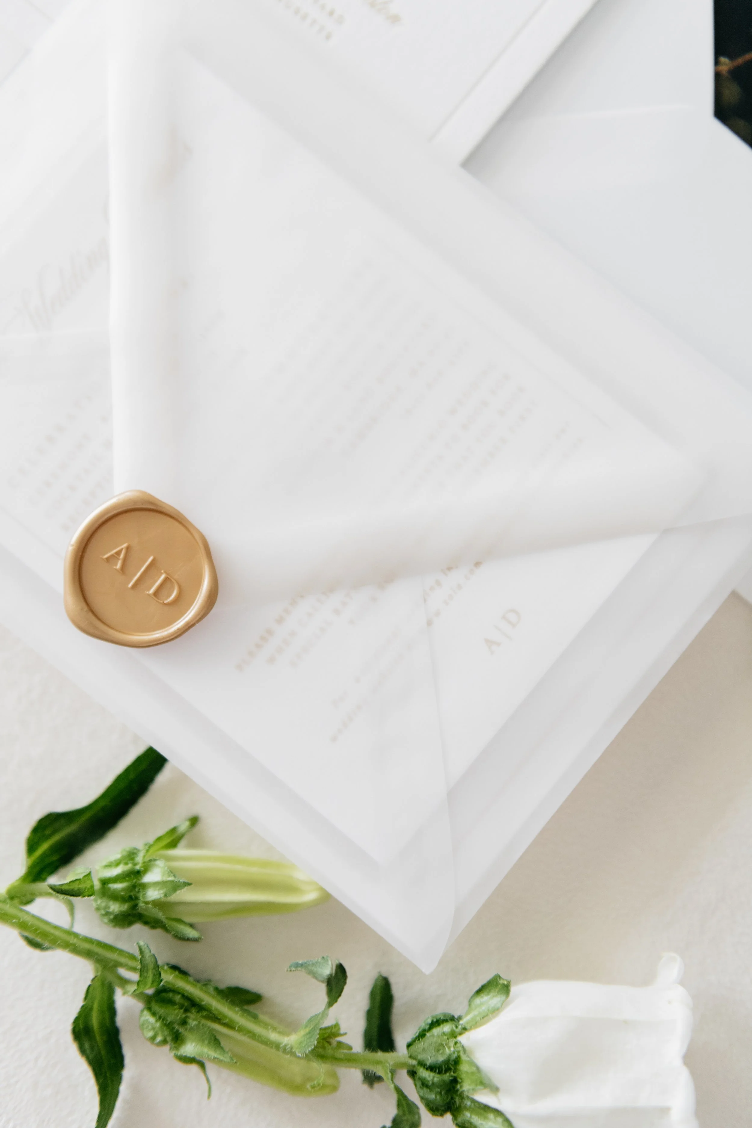 Elegant wedding invitation sealed with a gold wax stamp, featuring floral accents in the foreground.