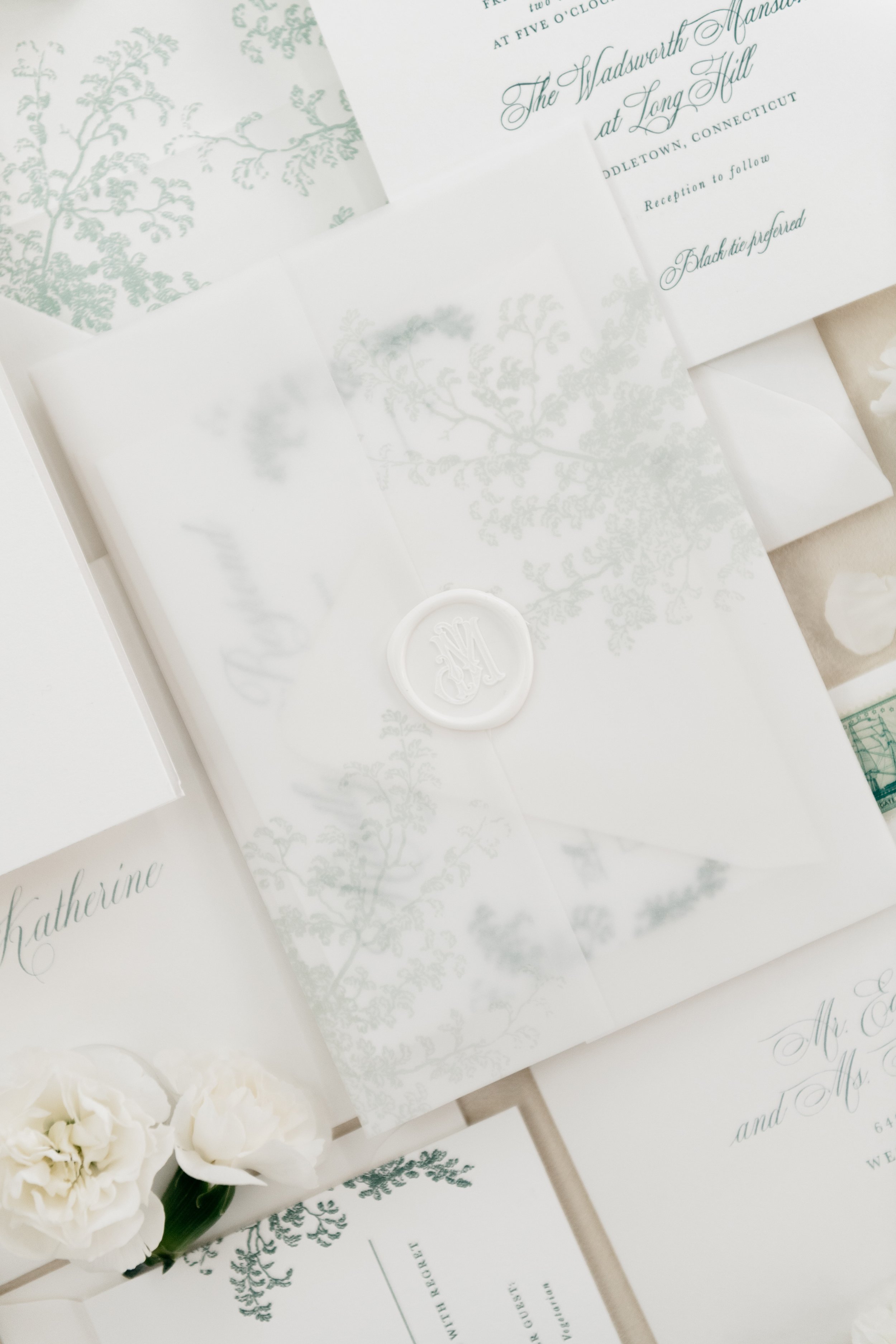 Elegant wedding invitations with floral designs, featuring a wax seal and delicate script. White flowers are placed nearby. Connecticut Weddings