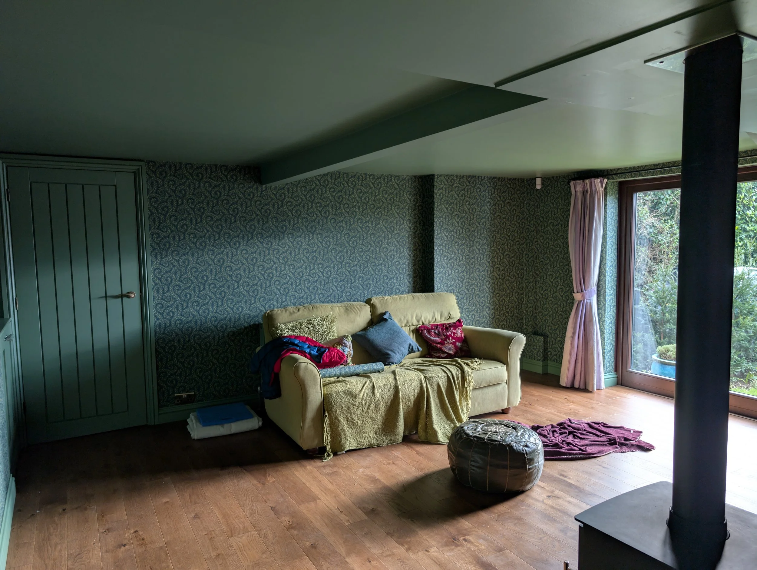 Residential living room with wooden floors, a cream sofa, and a black stove pipe, featuring premium green patterned wallpaper installed by West Sussex decorators.