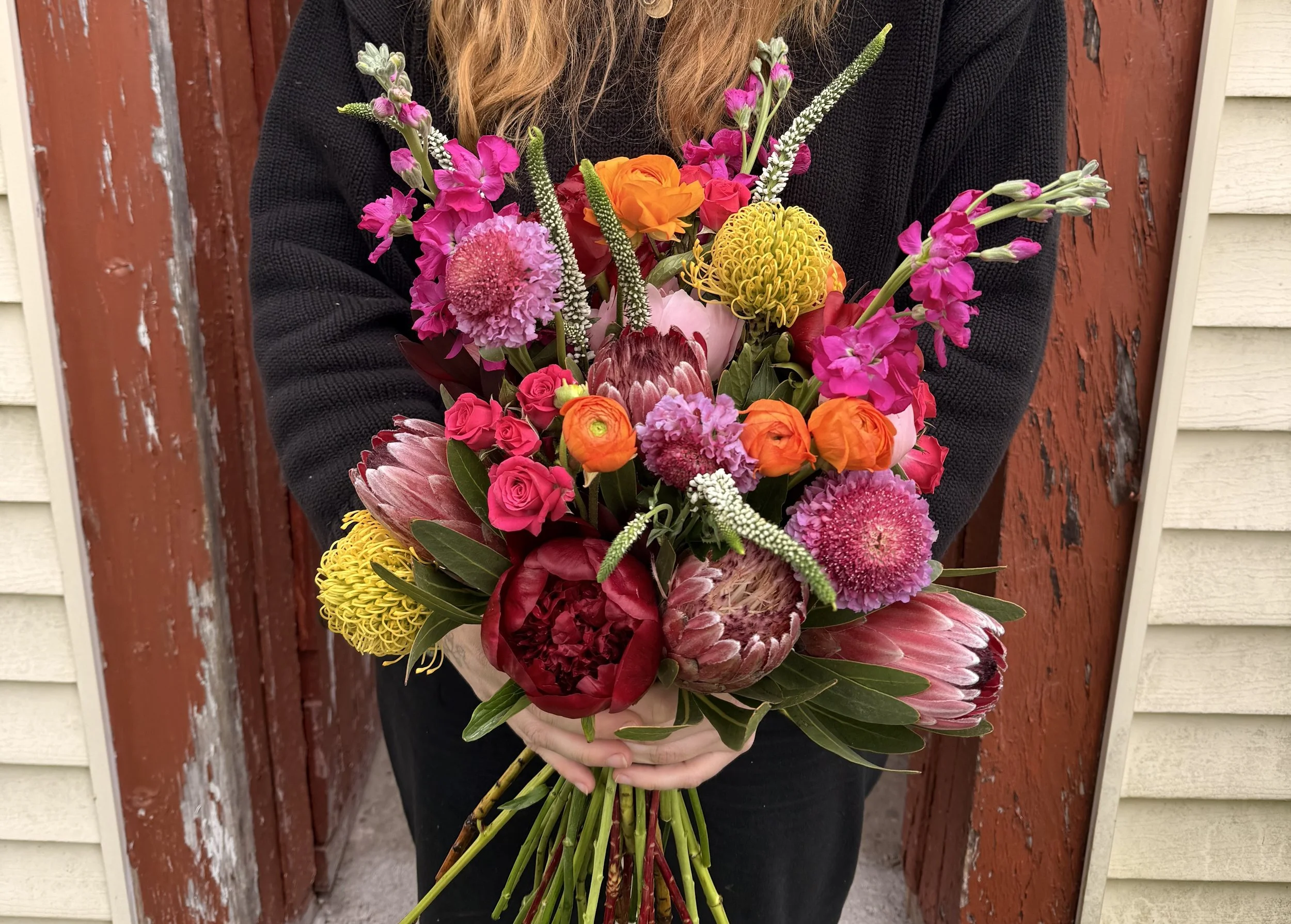 Person holding a bouquet of colorful flowers in front of a red and beige wooden wall.