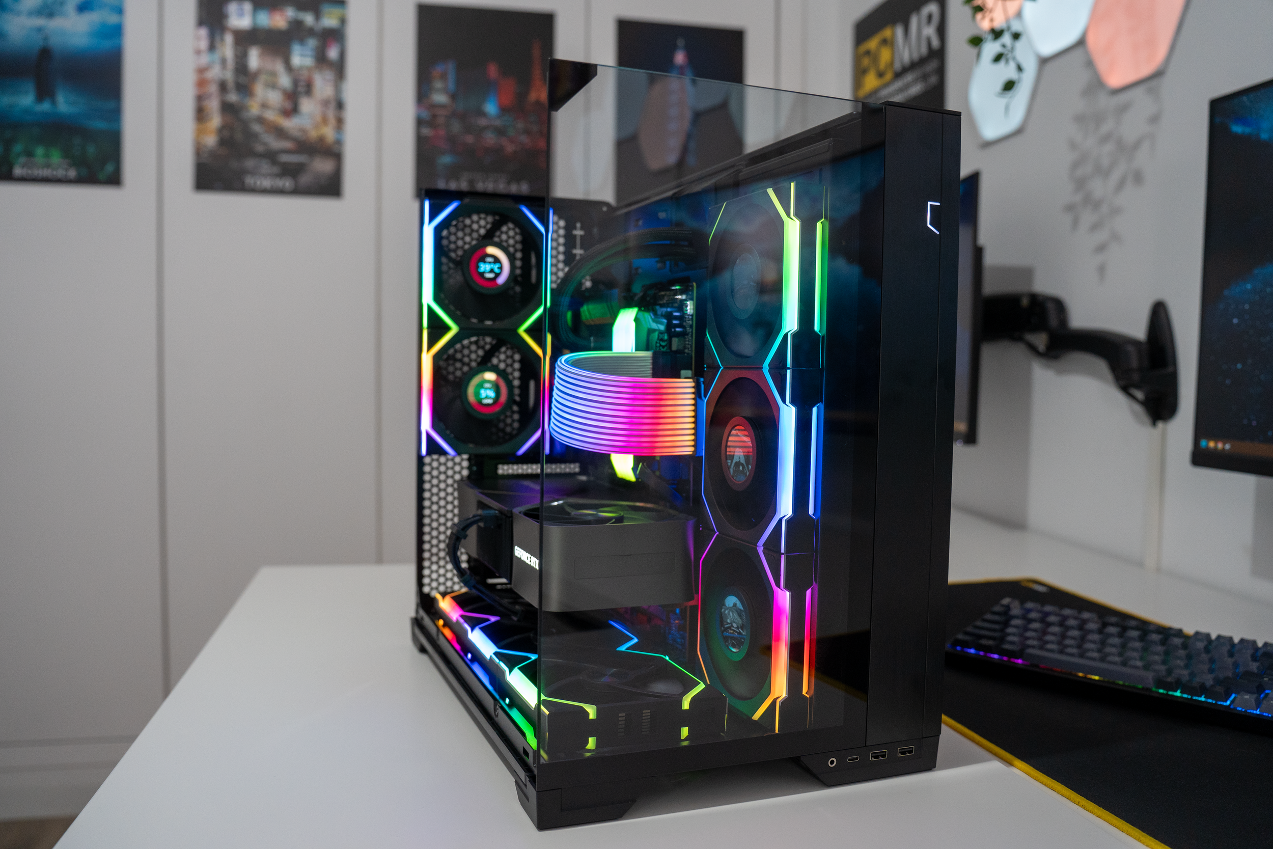 A desktop gaming PC with a glass side panel showing rainbow-colored LED lights and cooling fans, placed on a white table in a modern room.