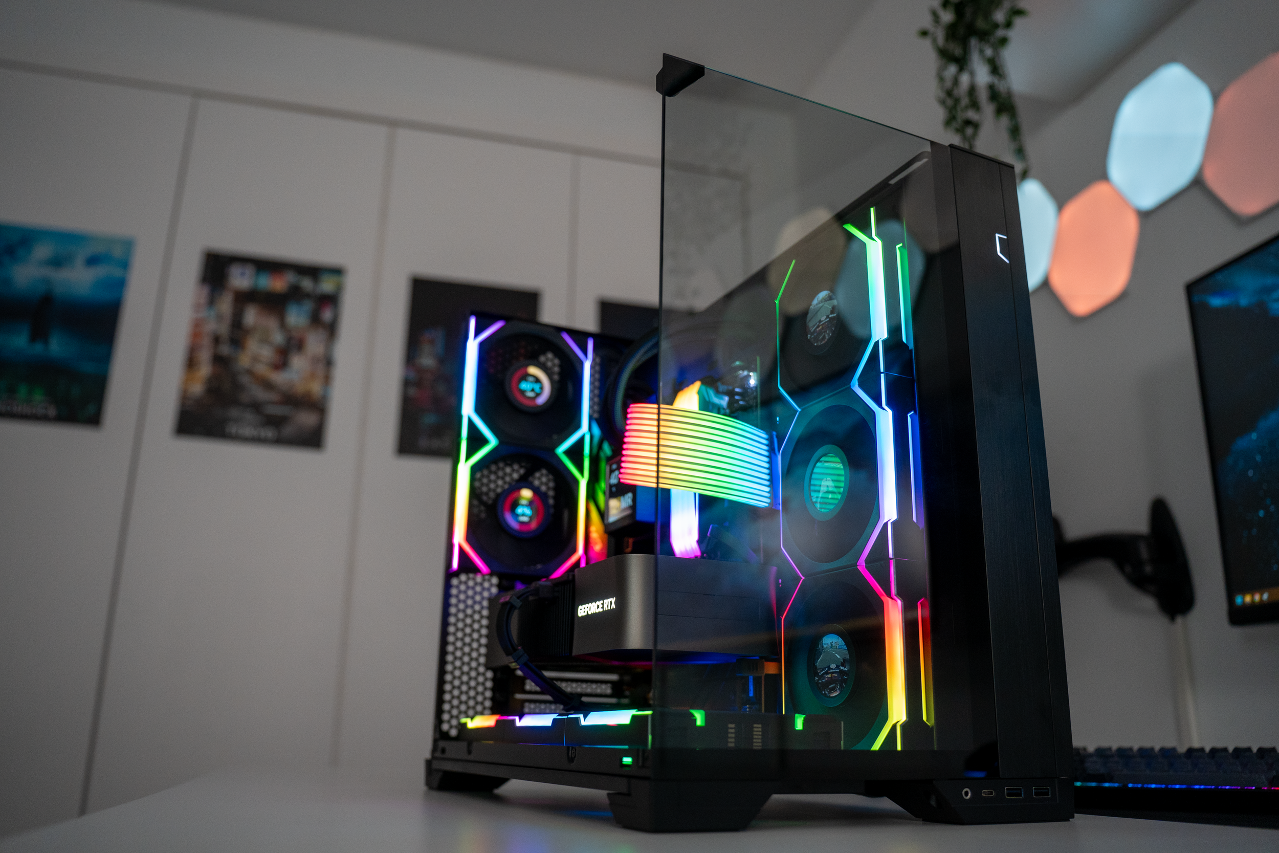 A gaming computer with a transparent side panel showing RGB lighting inside, including multiple cooling fans, a graphics card, and a CPU cooler, all illuminated with rainbow colors.