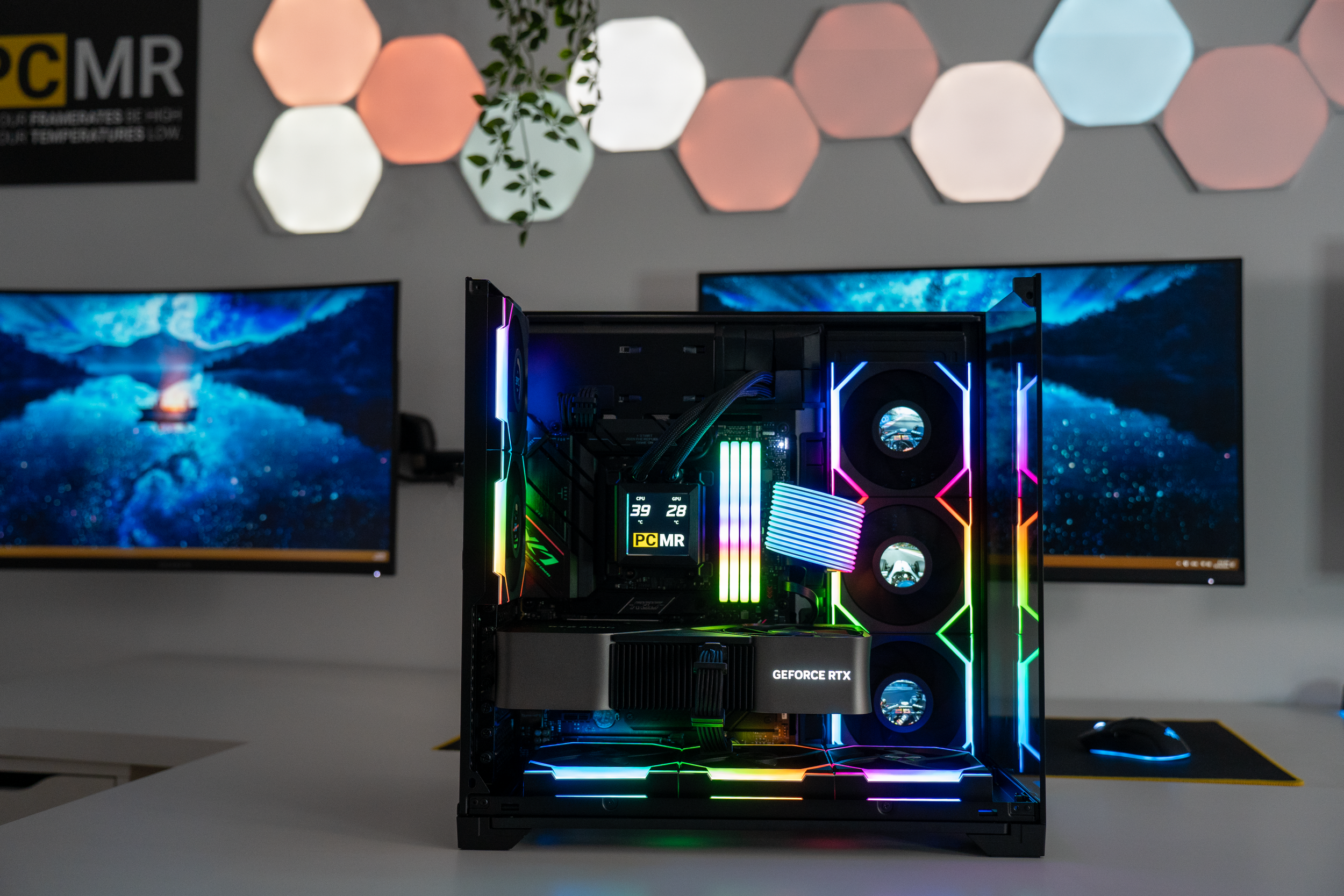 A gaming computer with RGB lighting inside a case, with two monitors showing a space-themed wallpaper, placed on a white desk.