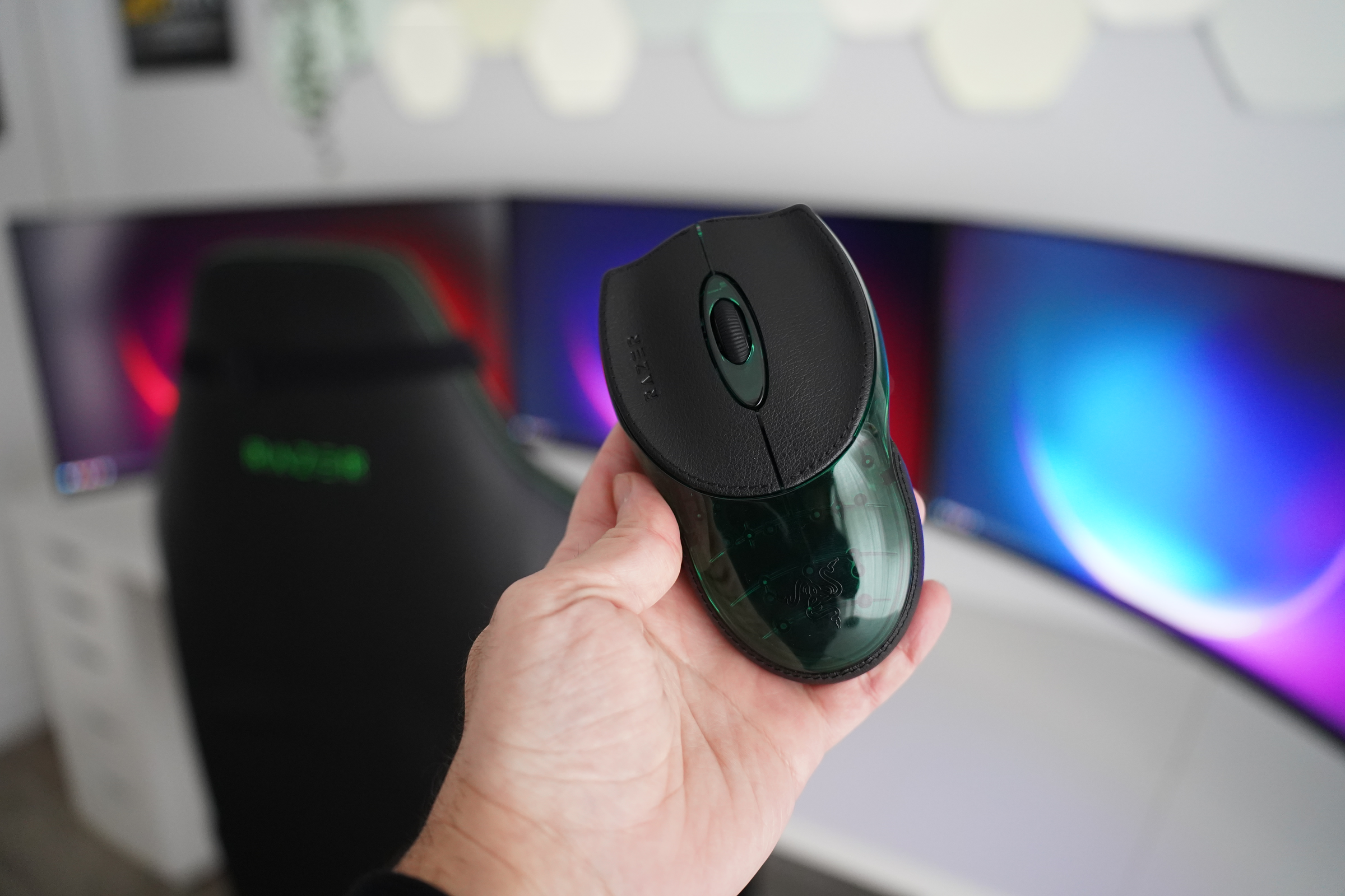 Person holding a razer mouse in front of three monitors with colorful screens.