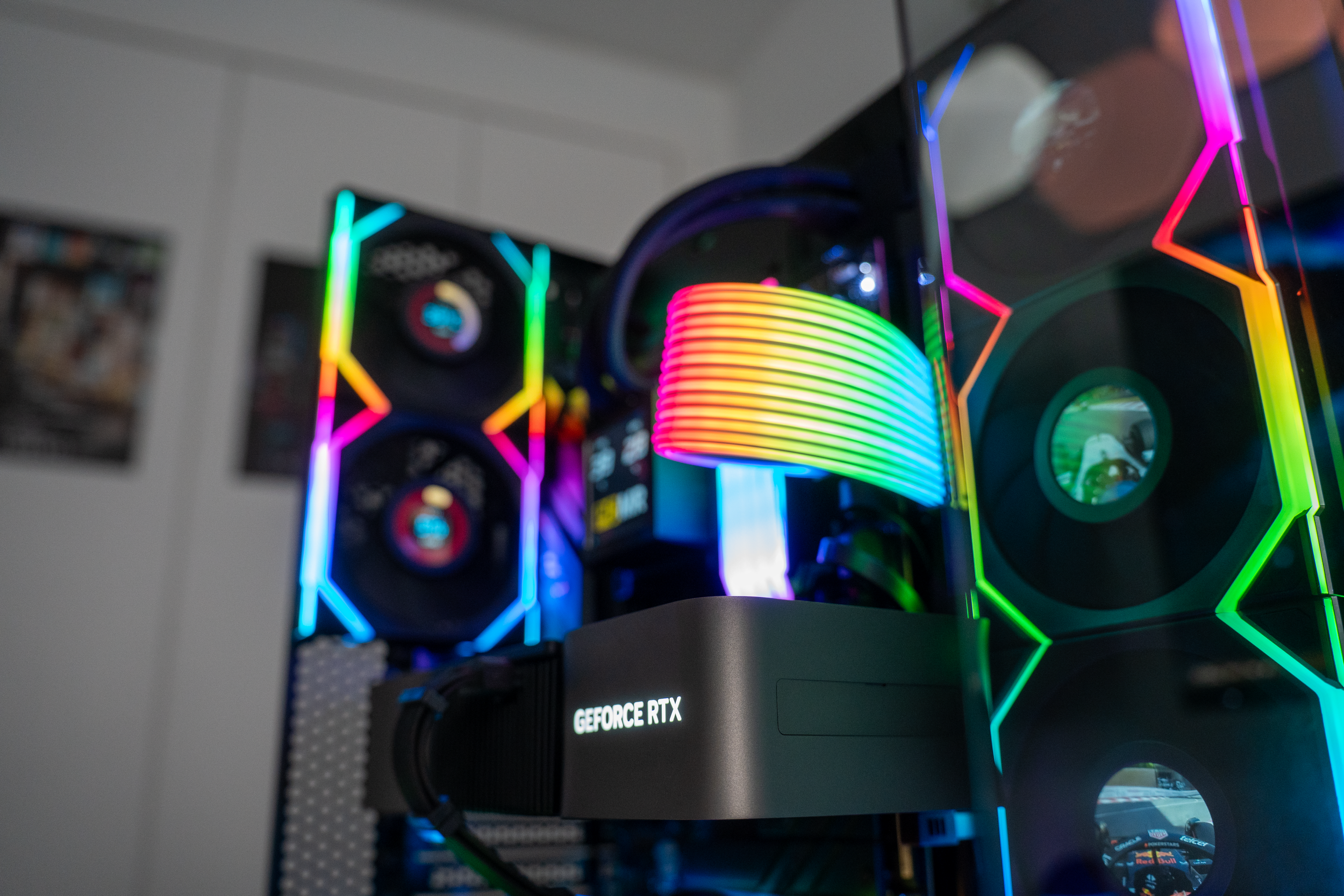 A close-up view of a custom-built gaming computer with a GeForce RTX graphics card, illuminated by colorful RGB lighting, inside a gaming setup.