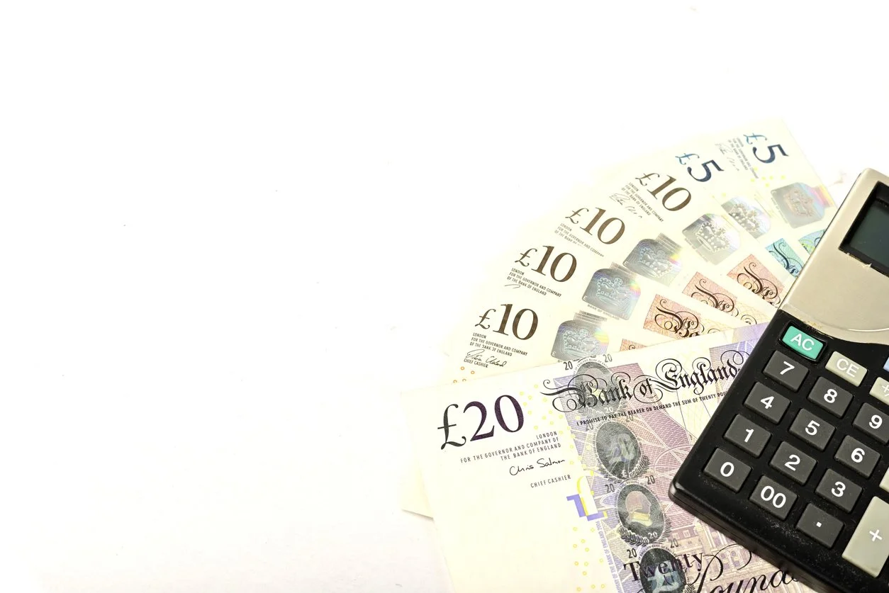 Various denominations of British currency banknotes and a calculator on a white surface.