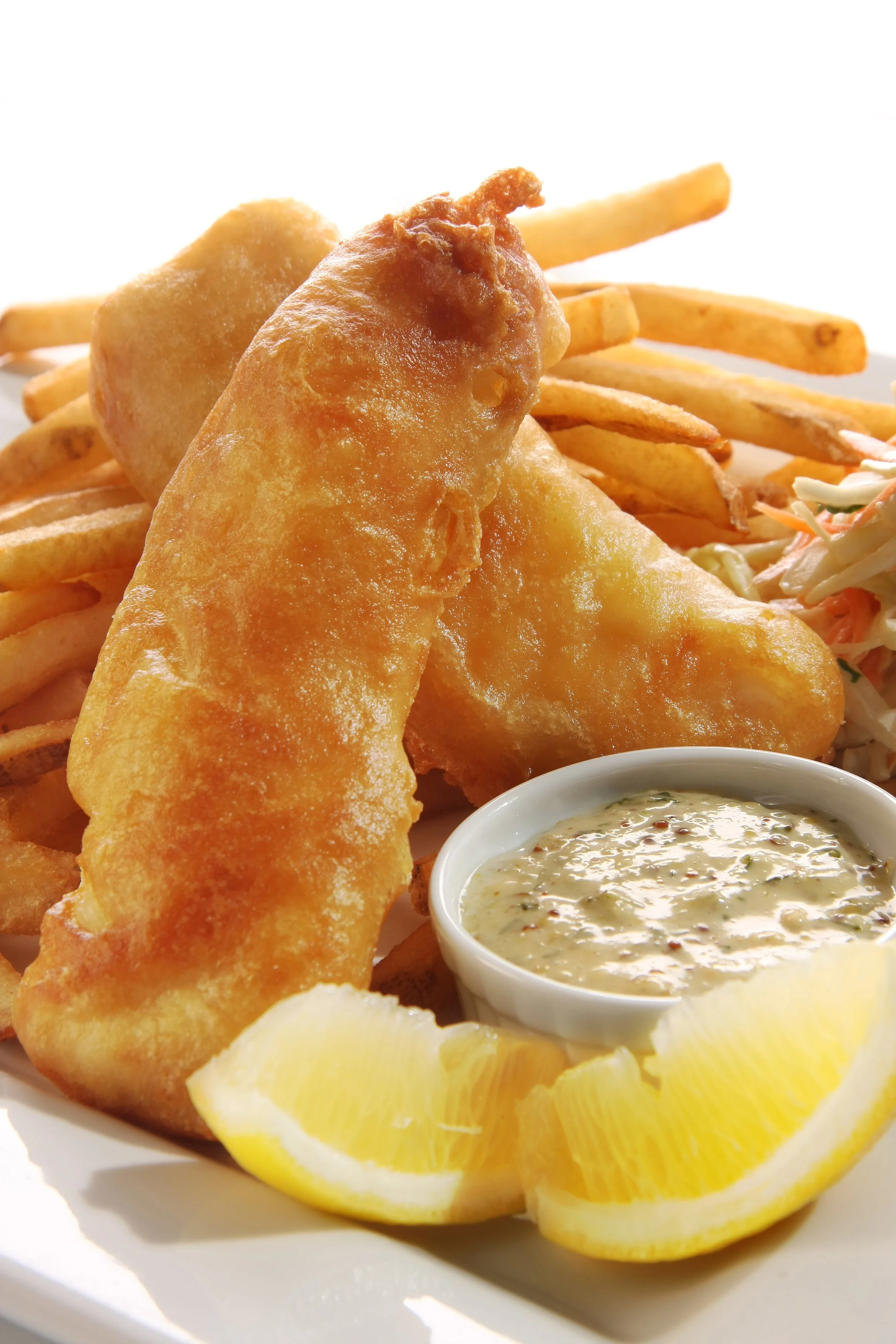 Plate of fried fish fillets with French fries, coleslaw, tartar sauce, and lemon wedges.