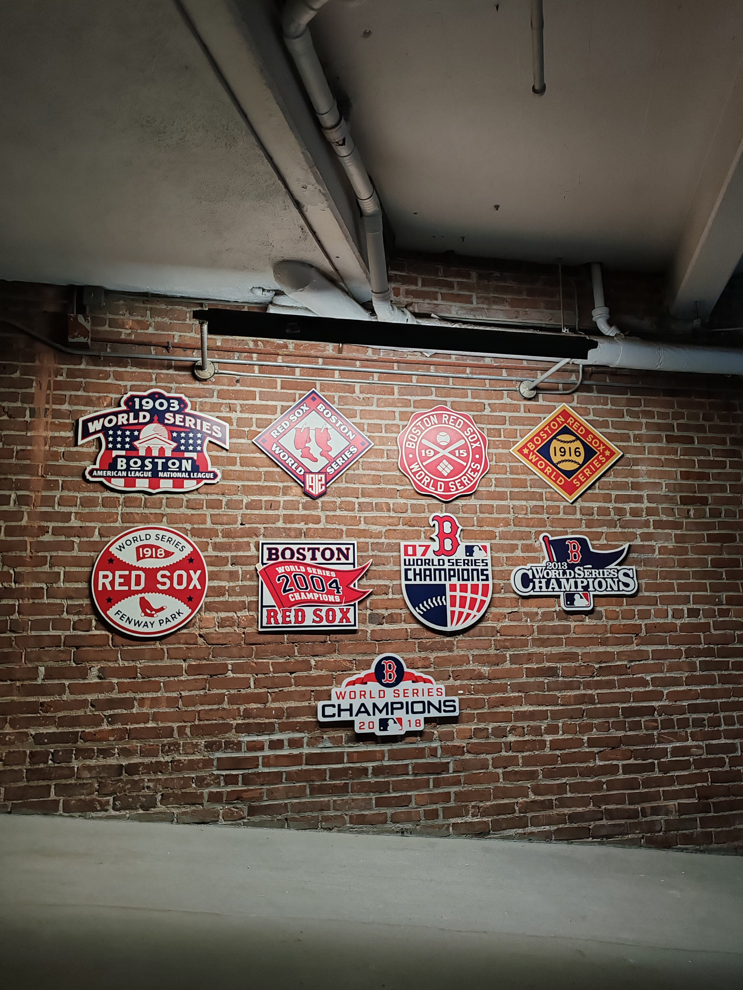 Panneaux de championnats des Red Sox de Boston accrochés sur un mur de briques; inclut les années 1903, 1912, 1915, 1916, 1918, 2004, 2007, 2013 et 2018, célébrant les victoires de la Série mondiale.