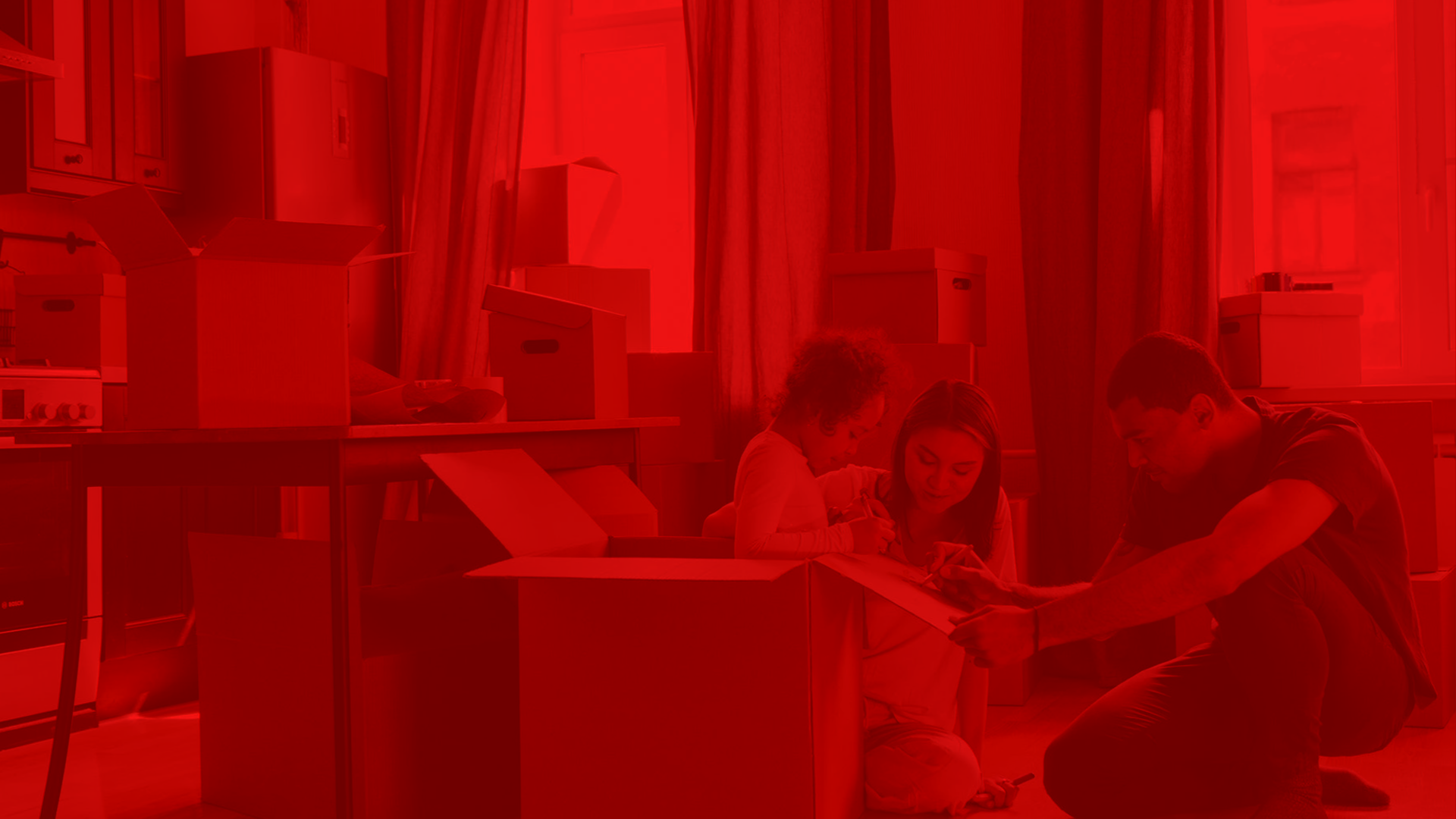 Three people, including a young girl, a young woman, and a young man, are sitting inside a room filled with cardboard boxes and storage containers, near a window with curtains, engaging with a tablet or similar device.