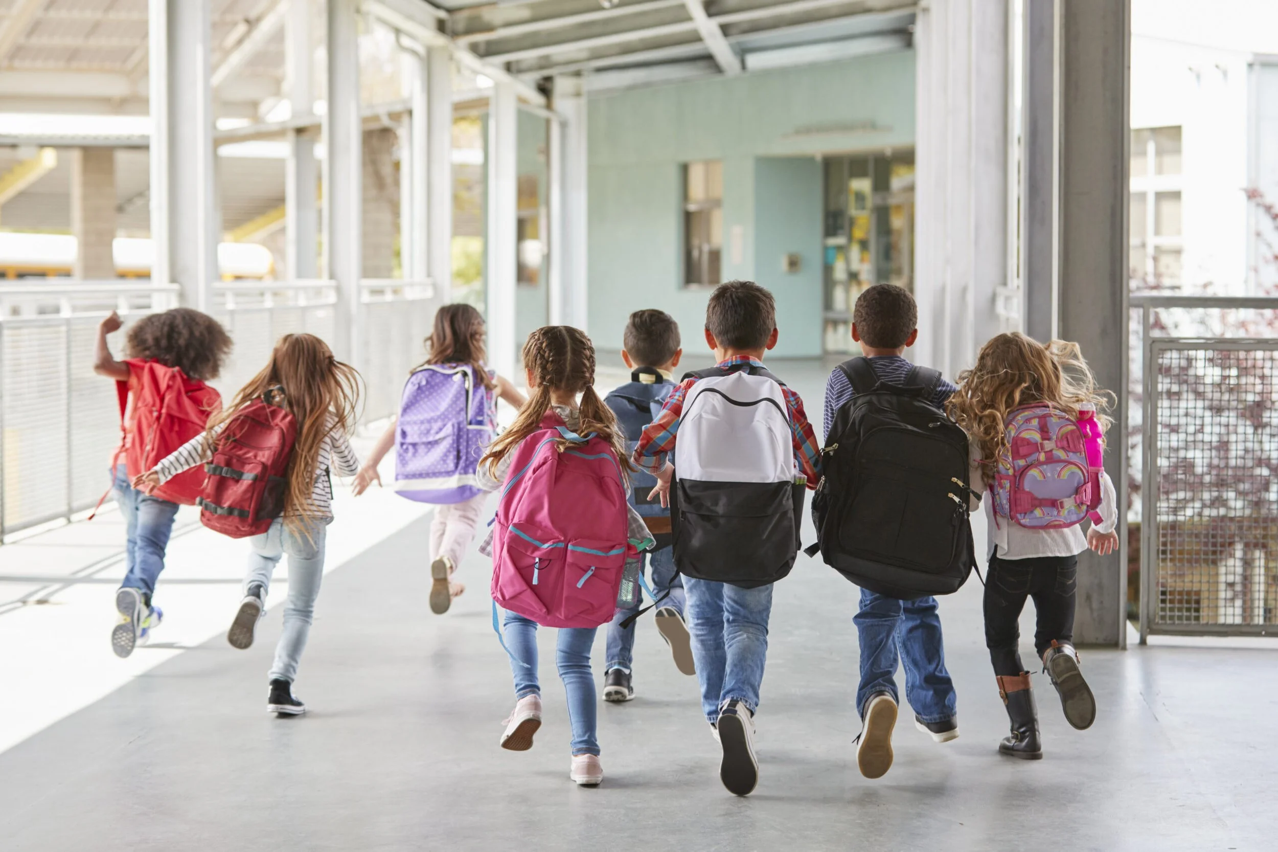 Group of children running with backpacks in a school corridor