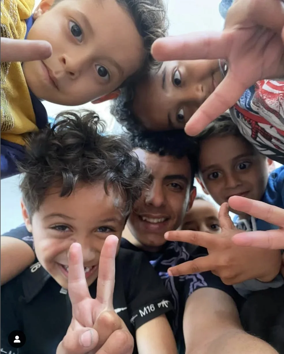 children with peace fingers in a circle around their dance teacher