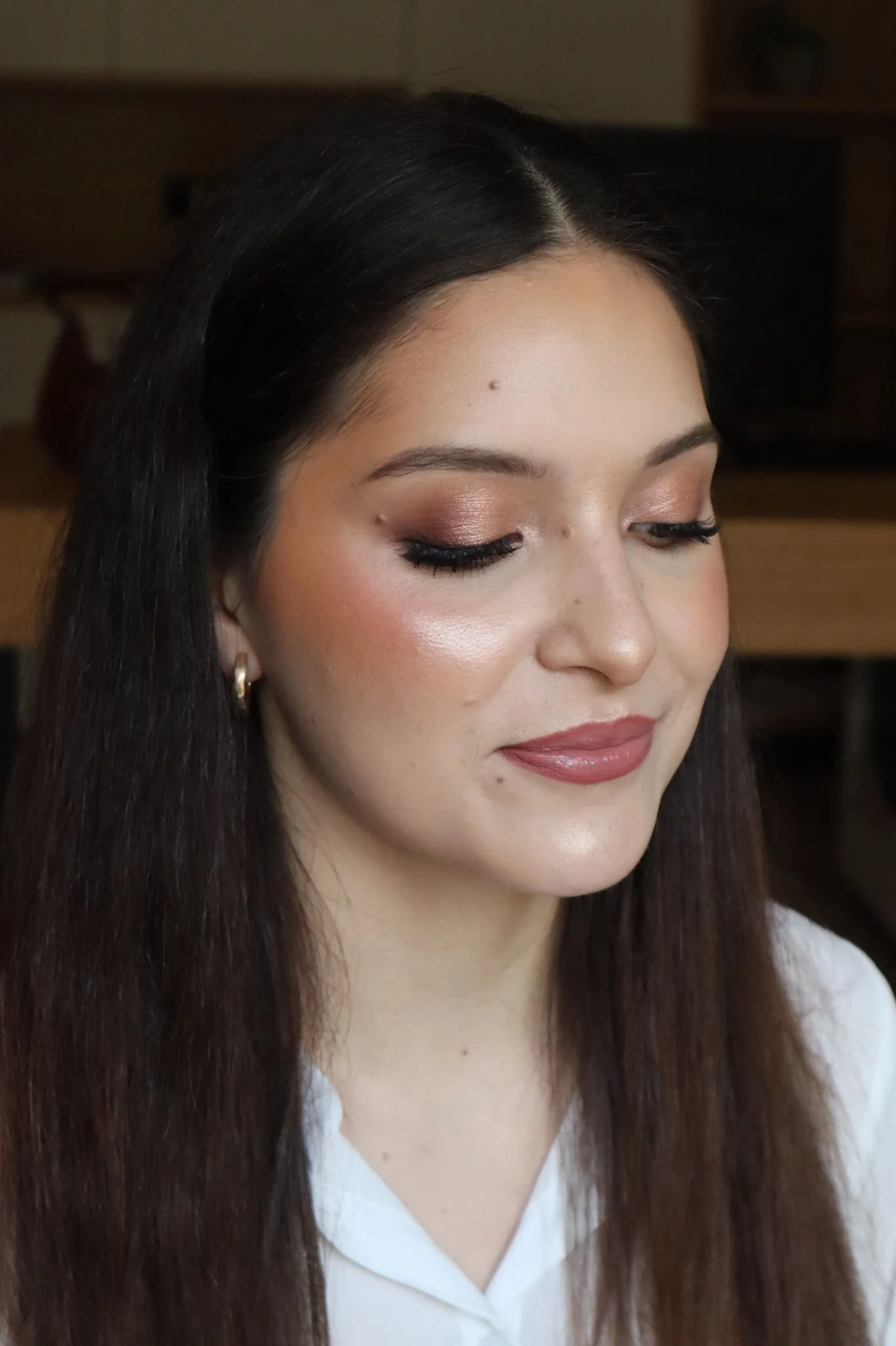 Mulher de cabelos longos e lisos, usando maquiagem com sombra marrom, batom rosado e pele iluminada.