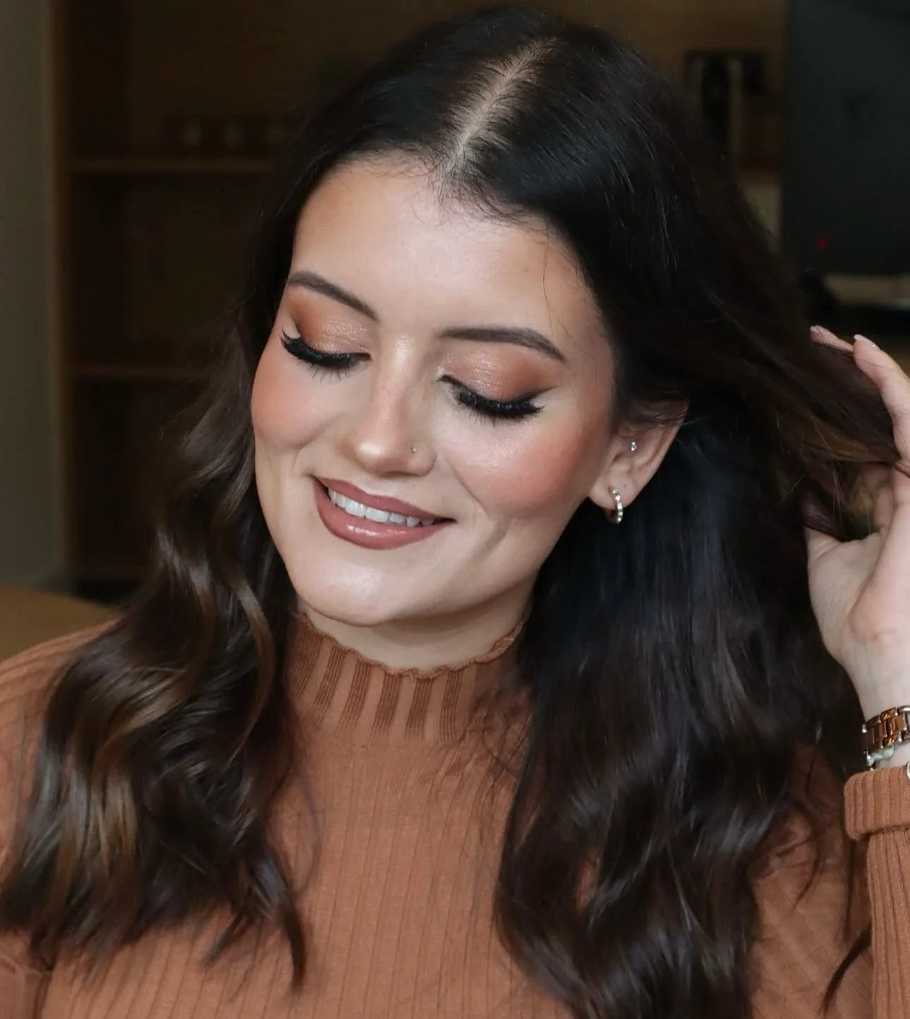 Mulher a sorrir com uma maquilhagem leve, cabelo castanho ondulado.