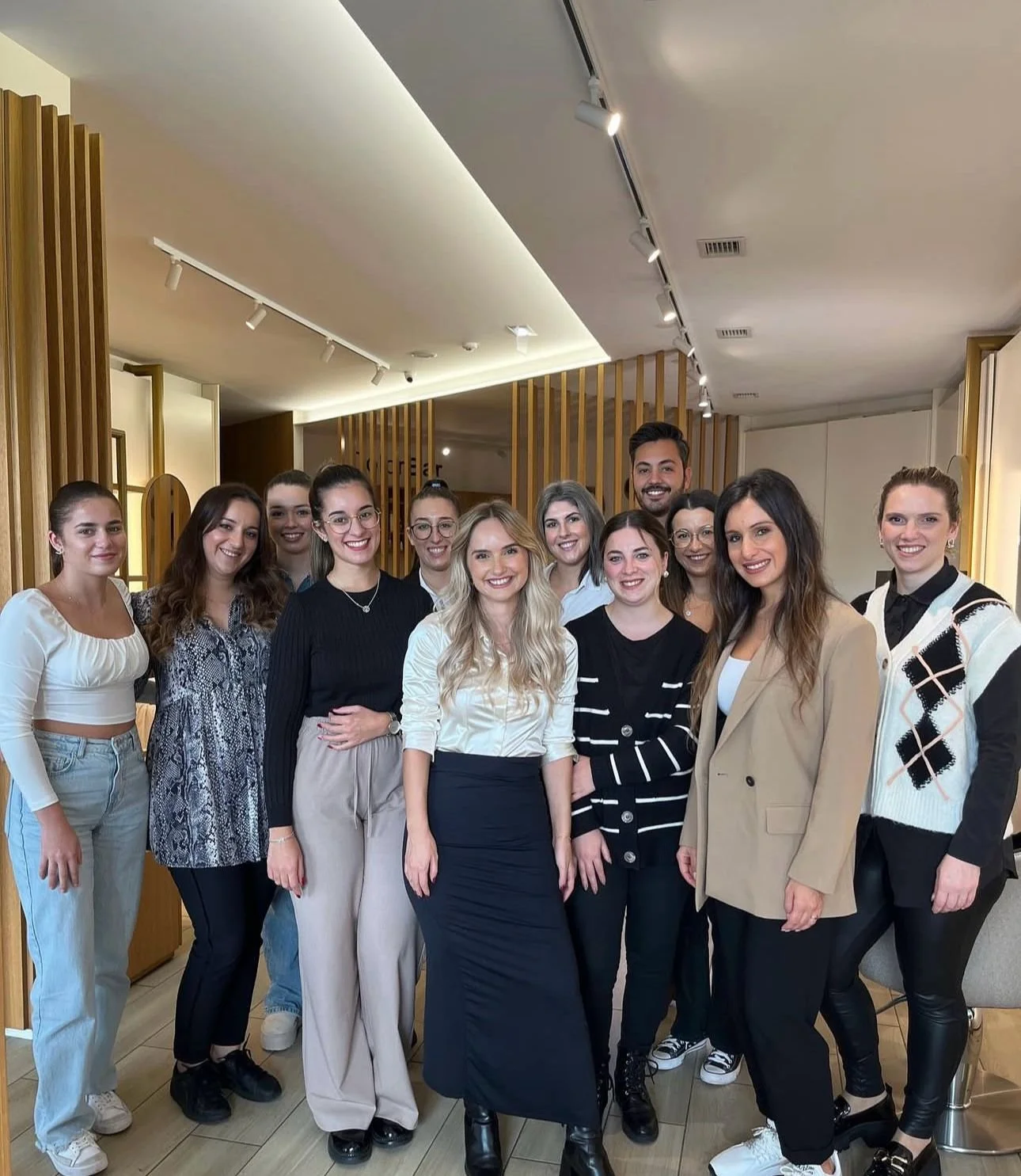 Grupo de 12 pessoas posando para foto em um ambiente interno bem iluminado, com decoração de madeira ao fundo. Todos estão sorrindo.