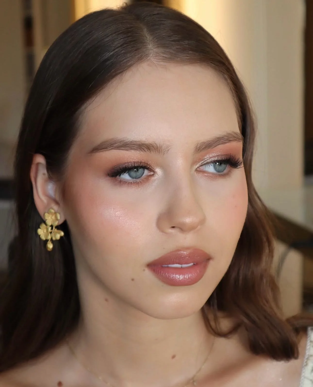 Mulher com uma maquiagem leve, olhos azuis, cabelo castanho, brincos dourados.