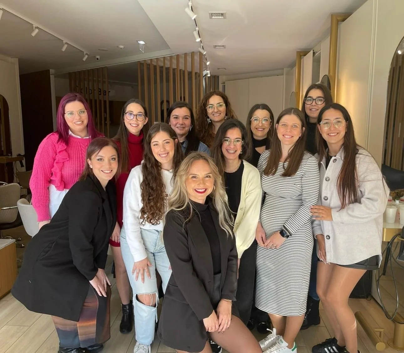 Grupo de mulheres posando para uma foto em um ambiente interno, todos sorrindo e vestindo roupas casuais.