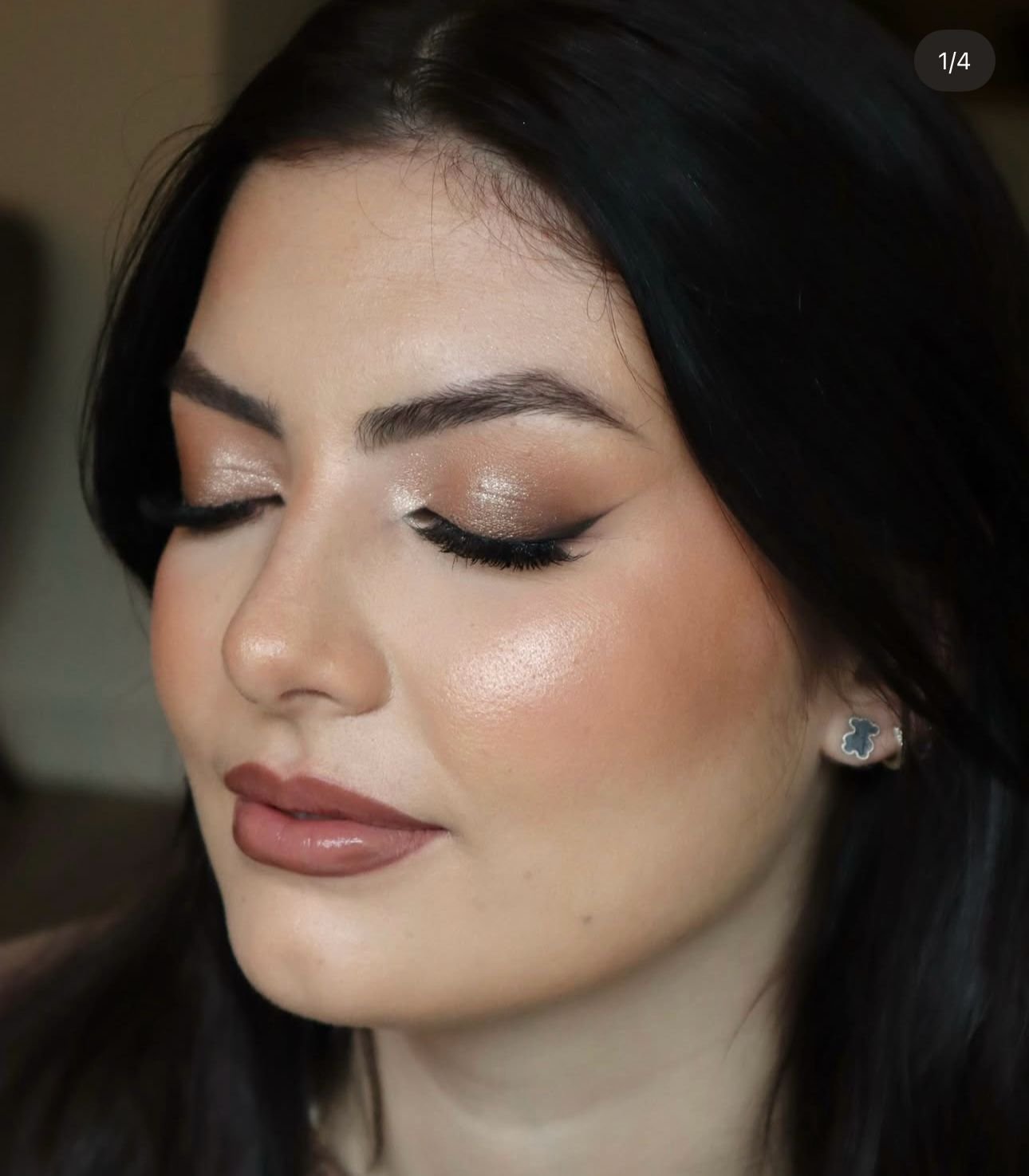 Mulher com maquilhagem sofisticada, olhos fechados, sombra com brilho, eyeliner, batom nude, cabelo escuro, brinco prateado.