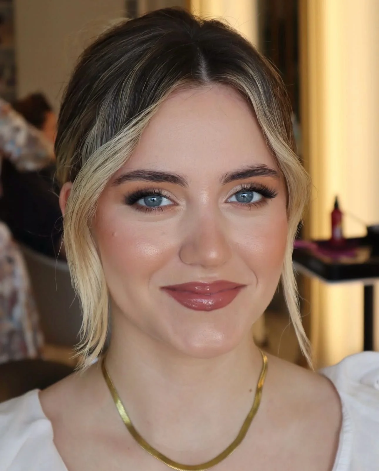 Mulher a sorrir, com cabelos claros presos, maquilhagem intensa que destaca os olhos azuis.