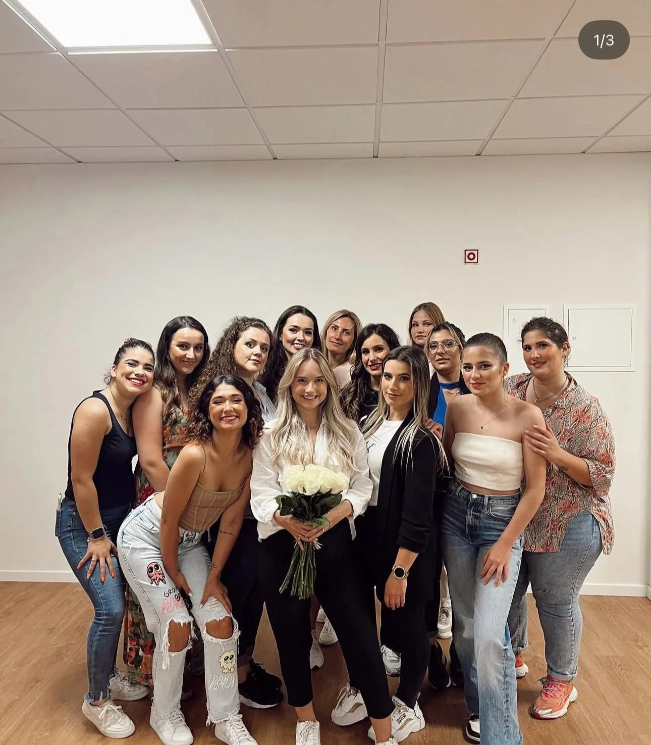 Grupo de mulheres a sorrir numa sala, com a Patricia Ferreira ao centro a segurar um ramo de flores brancas.