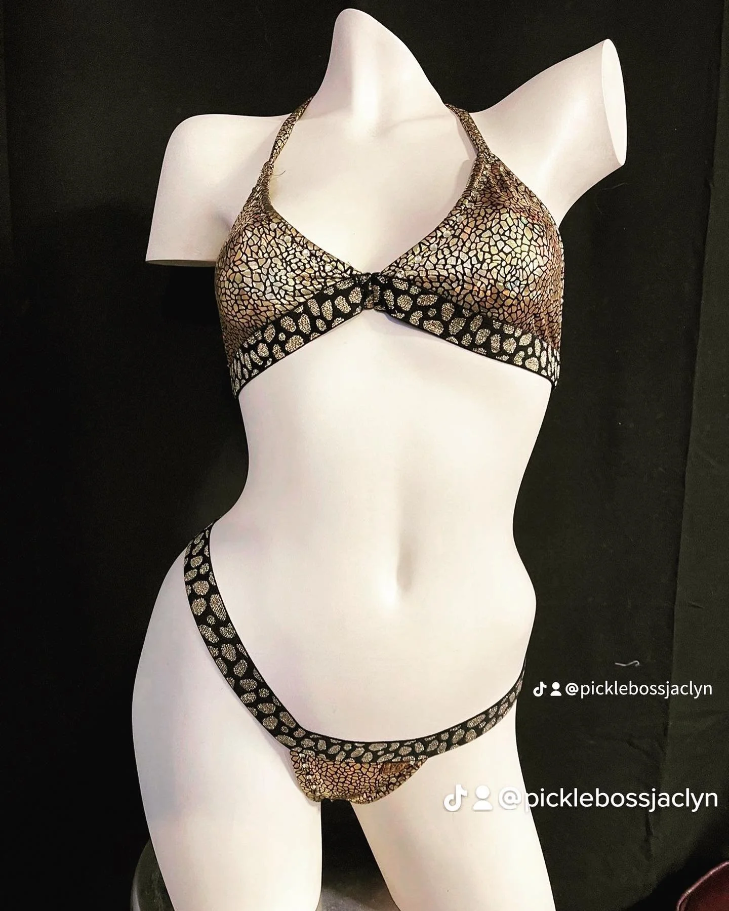 Mannequin wearing a snake print bikini with gold and black patterns against a black background.
