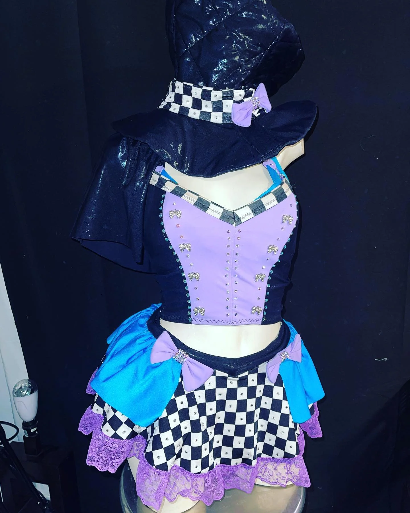 Mannequin wearing a colorful costume with a purple corset, checkered skirt, blue and purple bows, and a dark hood.