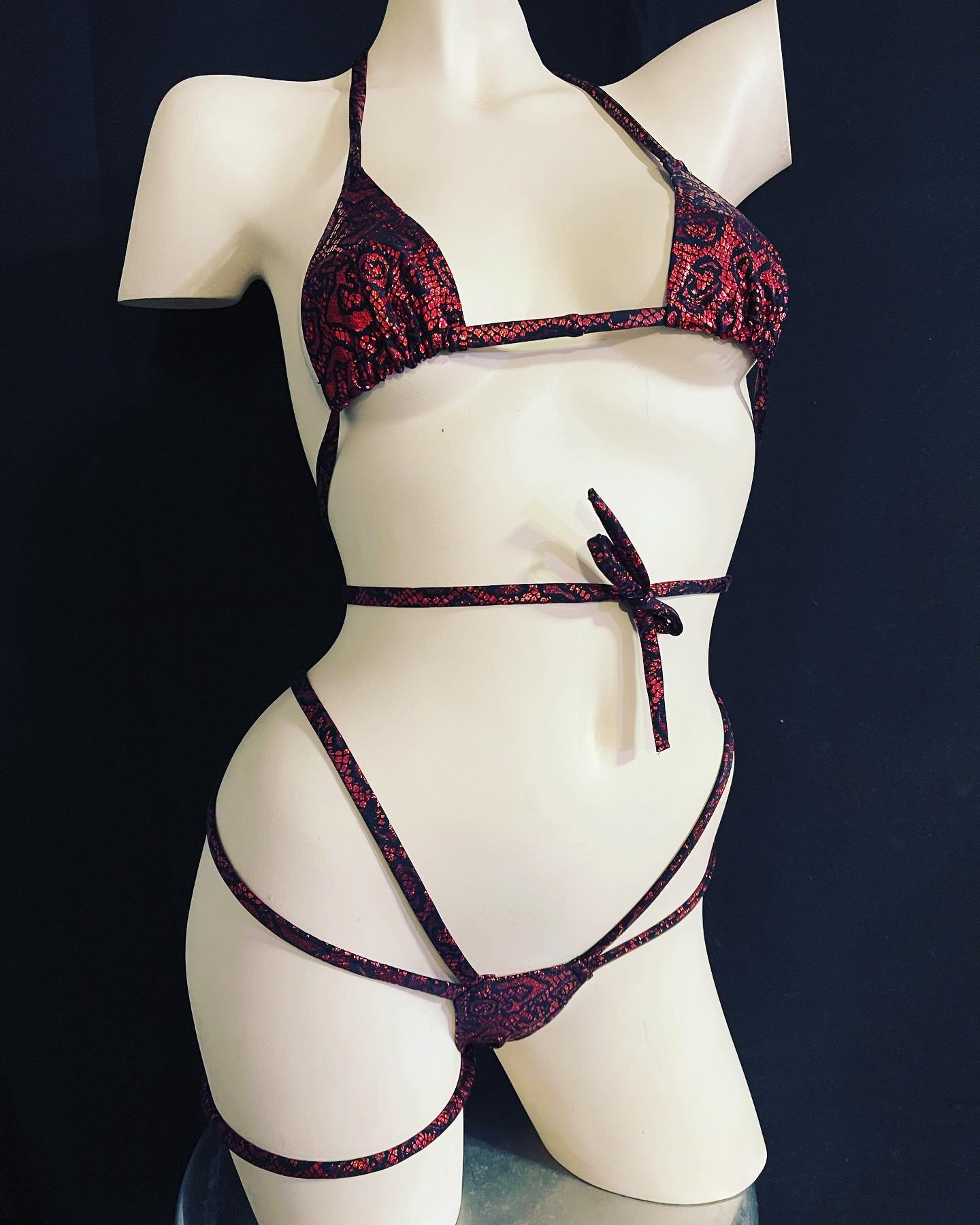 Mannequin wearing a strappy red and black bikini with a detailed lace pattern against a black background.