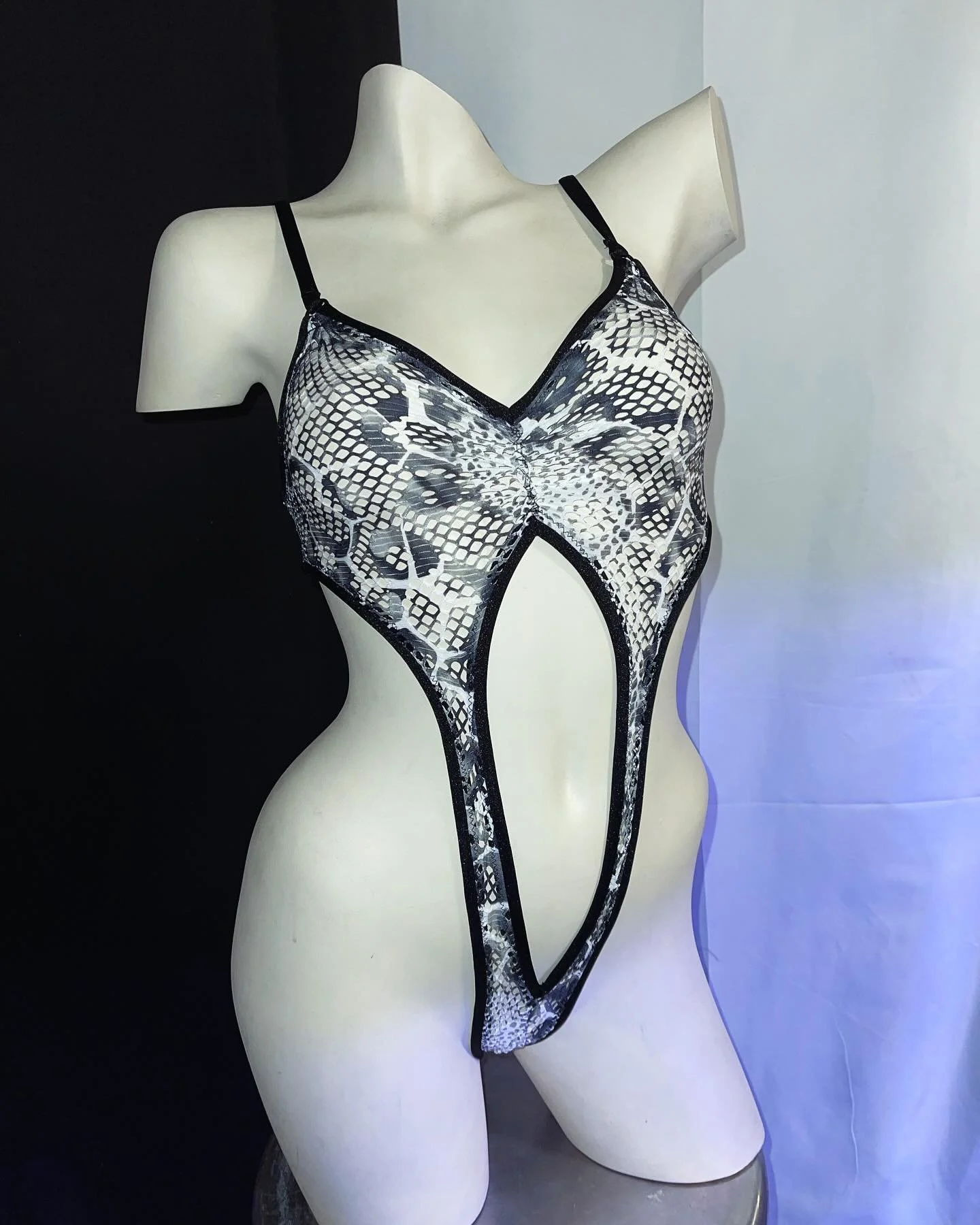 A white mannequin wearing a snake print, cut-out swimsuit with spaghetti straps.