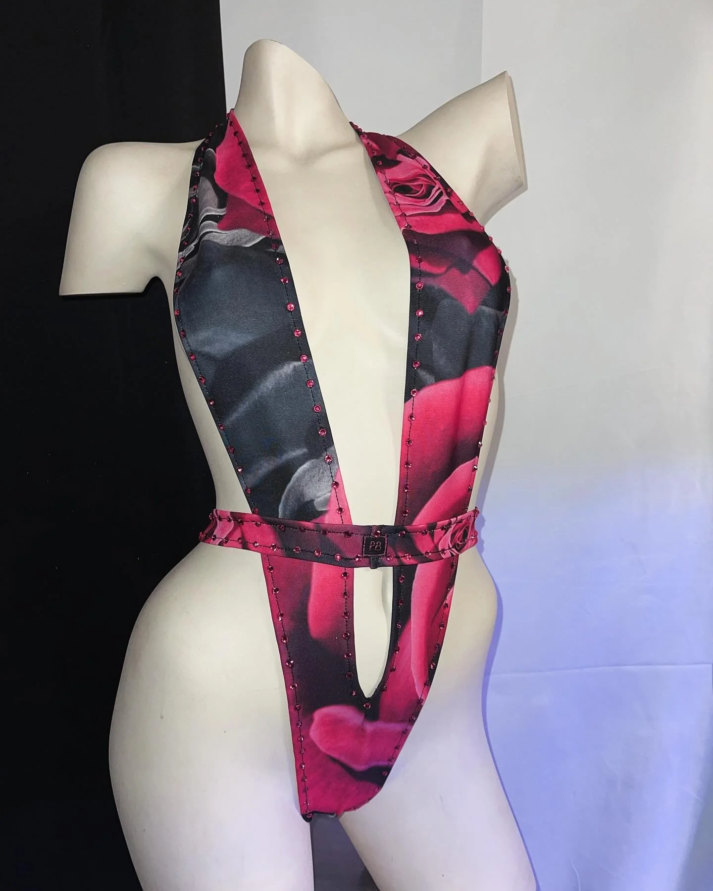 Mannequin wearing floral patterned pink and black halter swimsuit with deep neckline and cutouts, set against a black and white background.