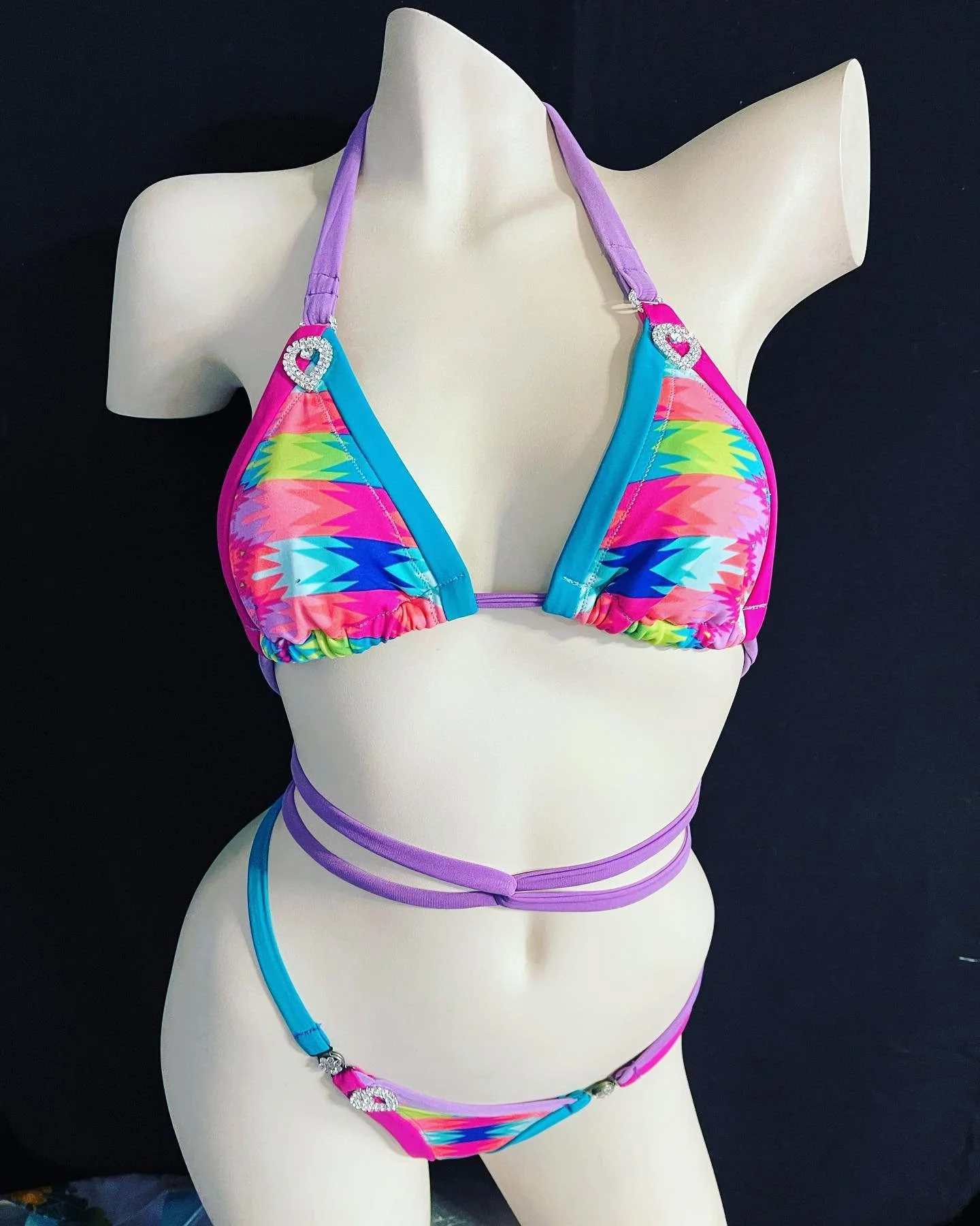 Colorful geometric-patterned bikini on mannequin with purple straps and heart-shaped embellishments.