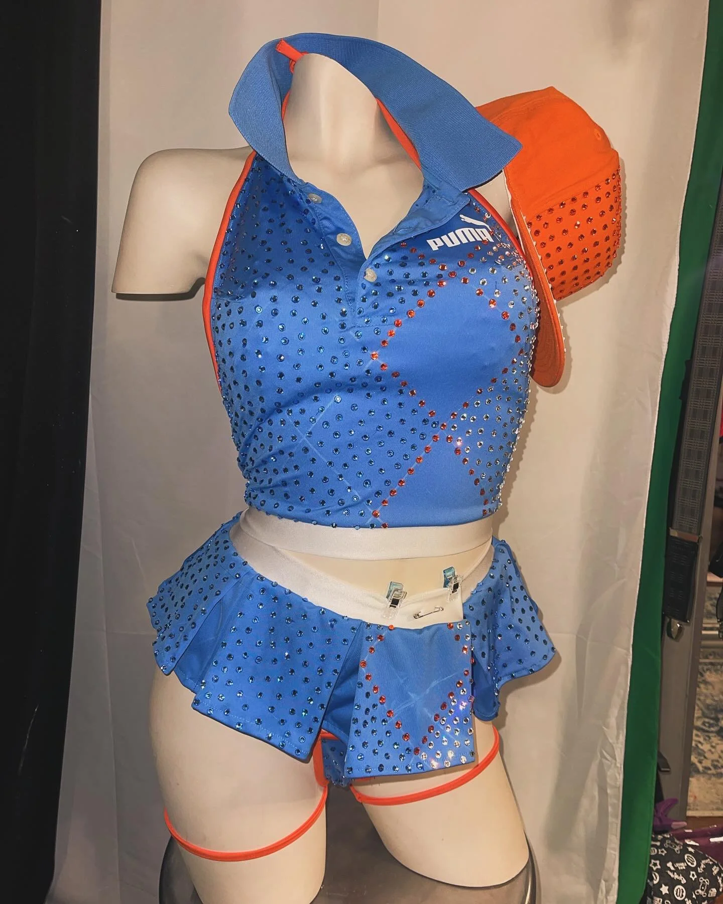 Mannequin wearing a blue and orange rhinestone-studded sports outfit with a crop top and skirt, accompanied by an orange cap.