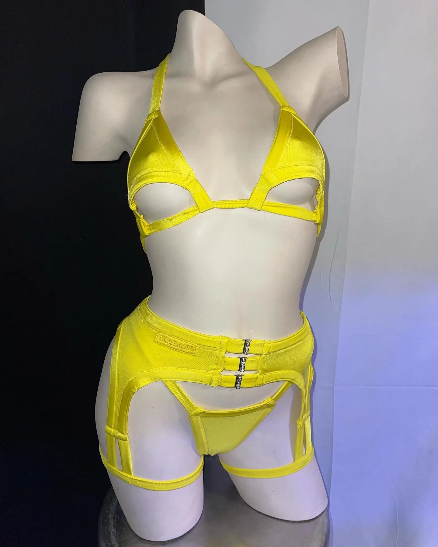 Mannequin wearing bright yellow lingerie set with harness details on a neutral background.