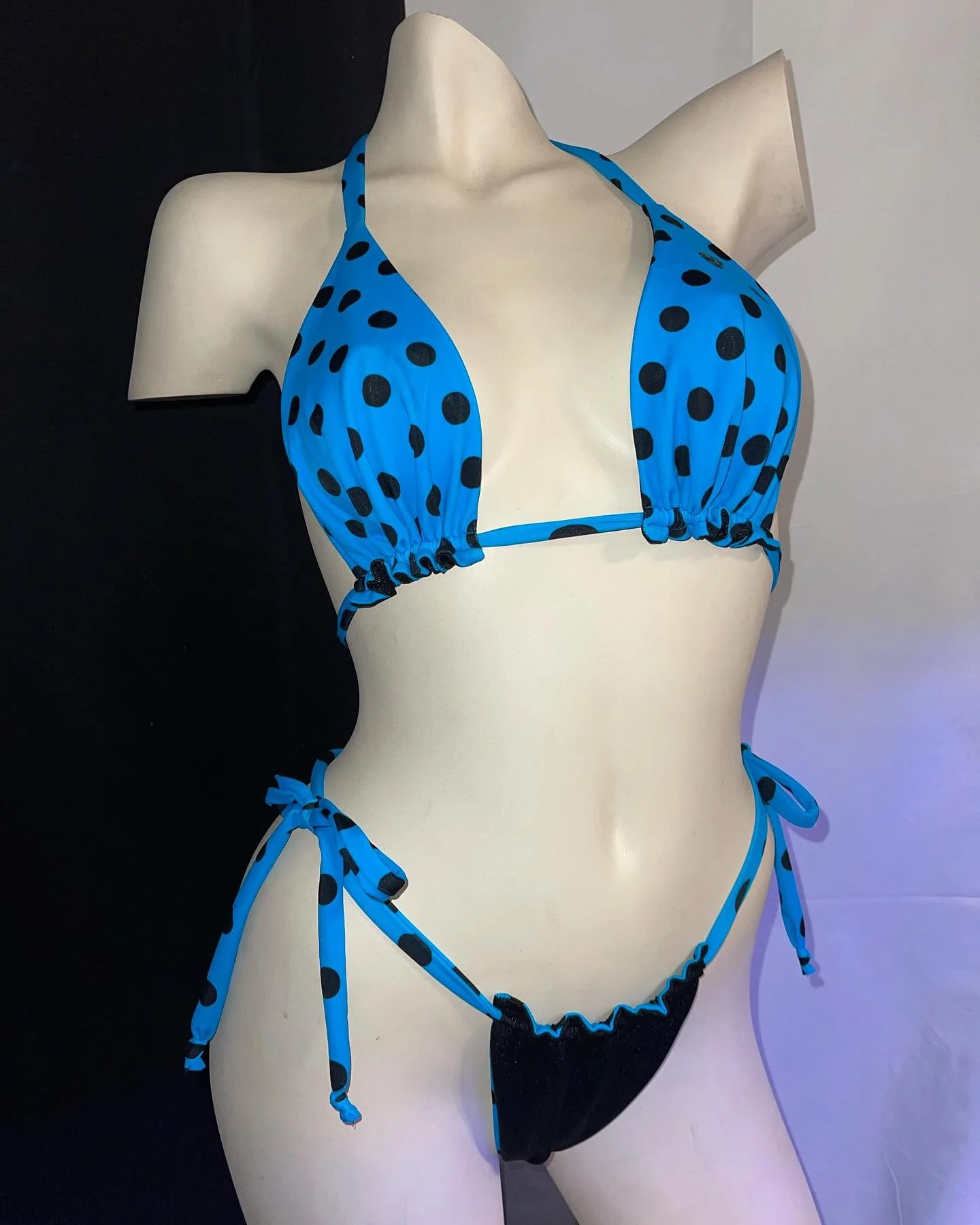 Mannequin wearing a blue polka dot bikini against a white and black background.