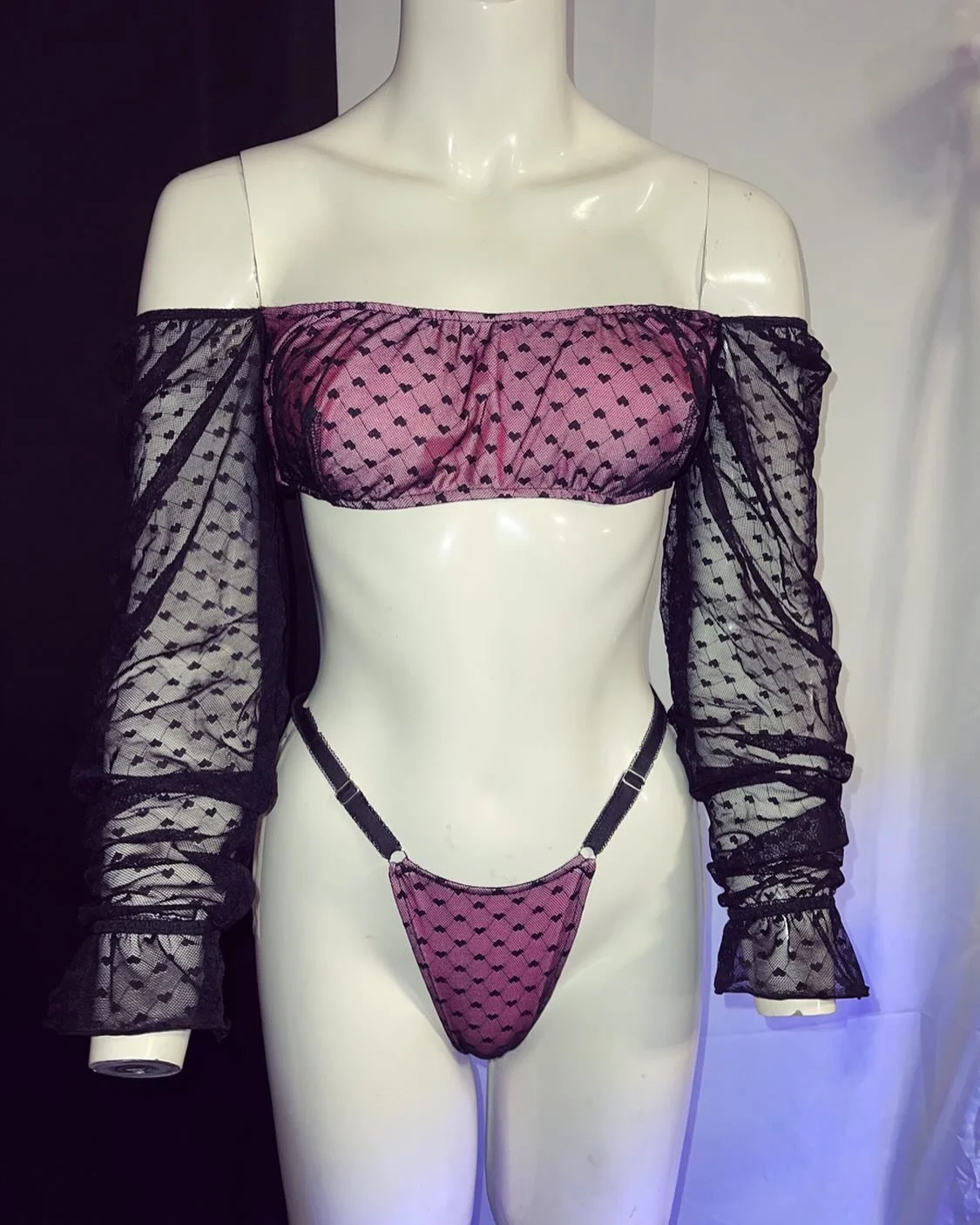 Mannequin wearing a sheer black and purple lingerie set with off-the-shoulder sleeves and heart pattern.