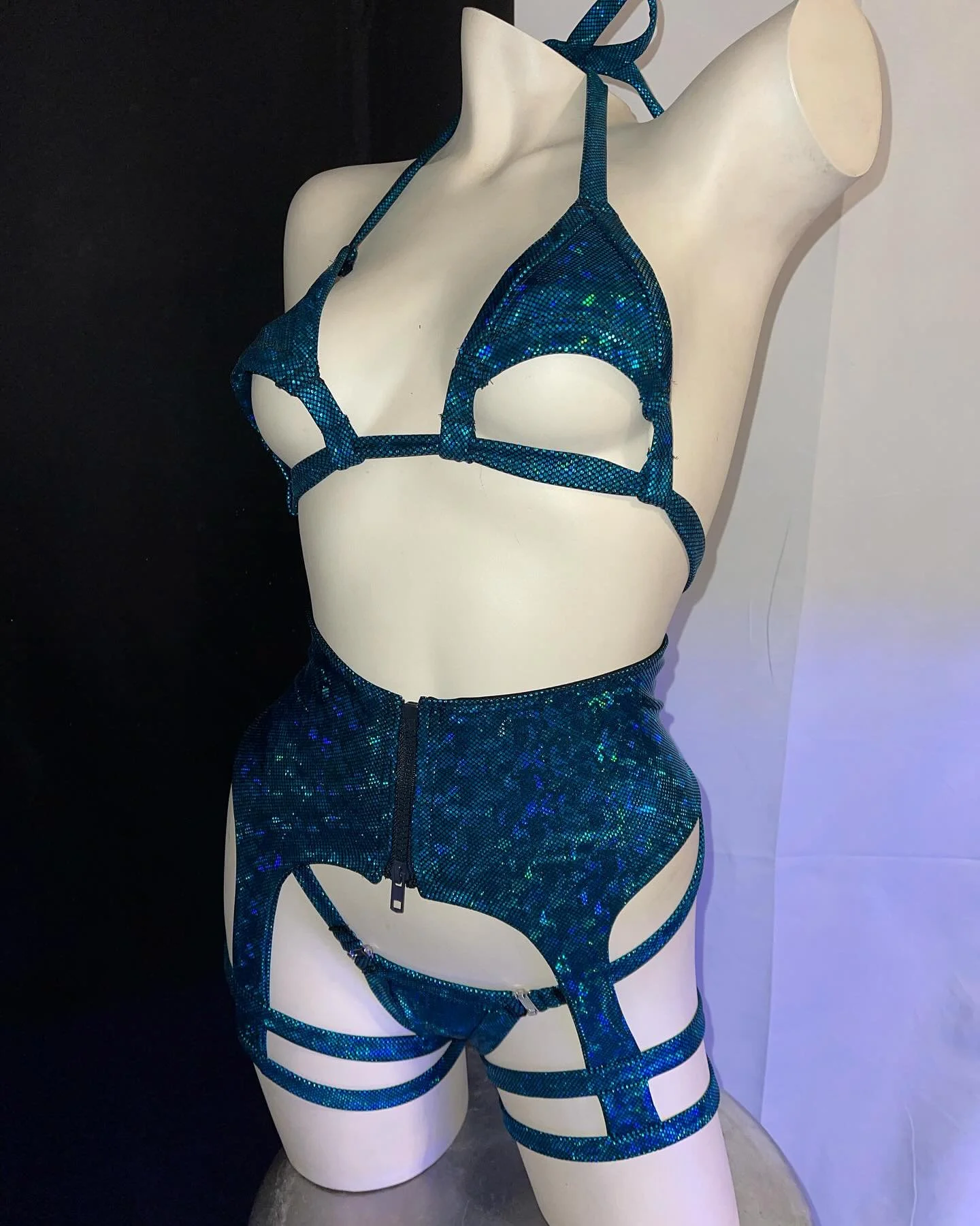 A mannequin wearing a strappy blue iridescent bikini set with matching high-waisted bottoms and thigh straps.