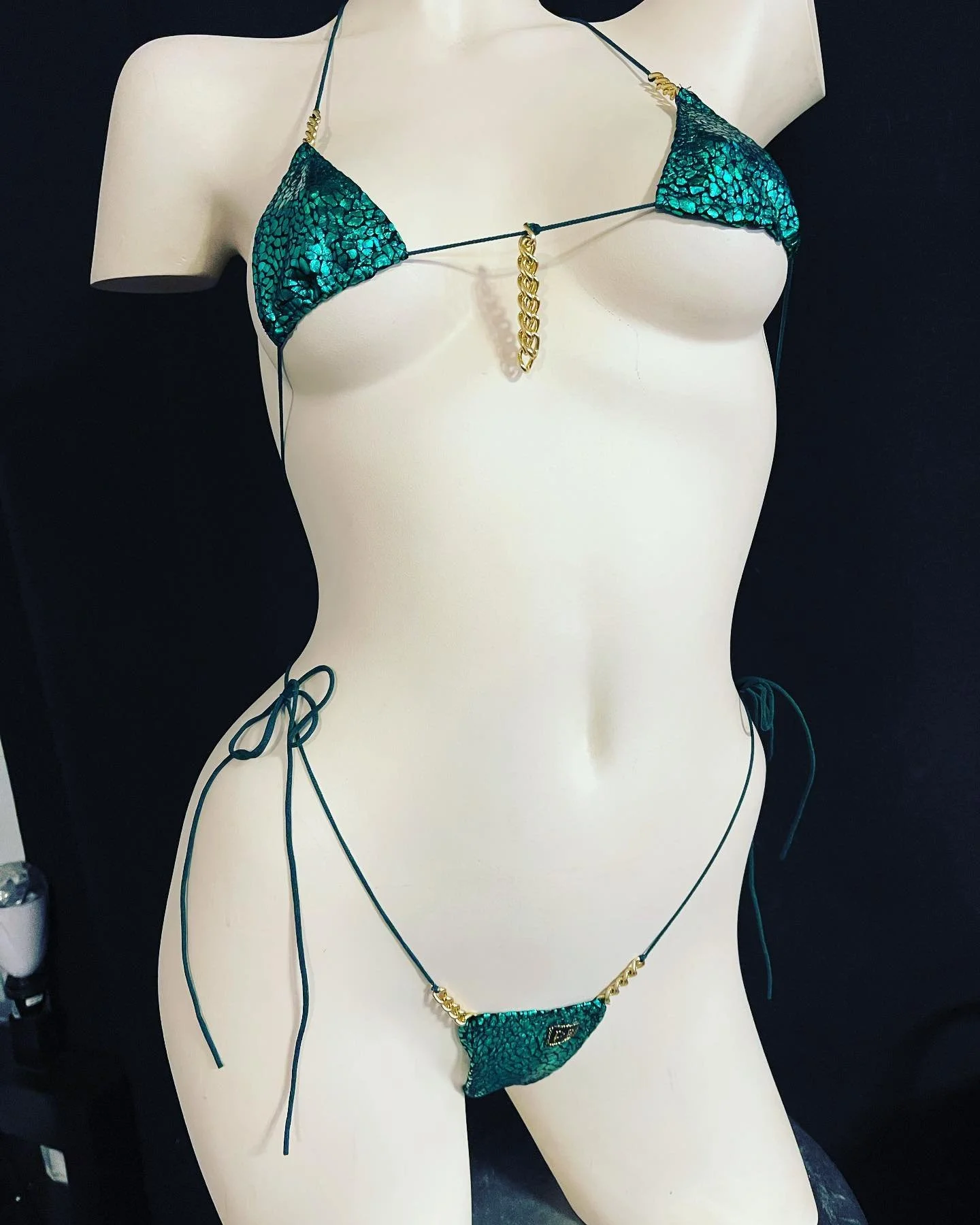 Mannequin wearing a green bikini with gold chain accents, black background.