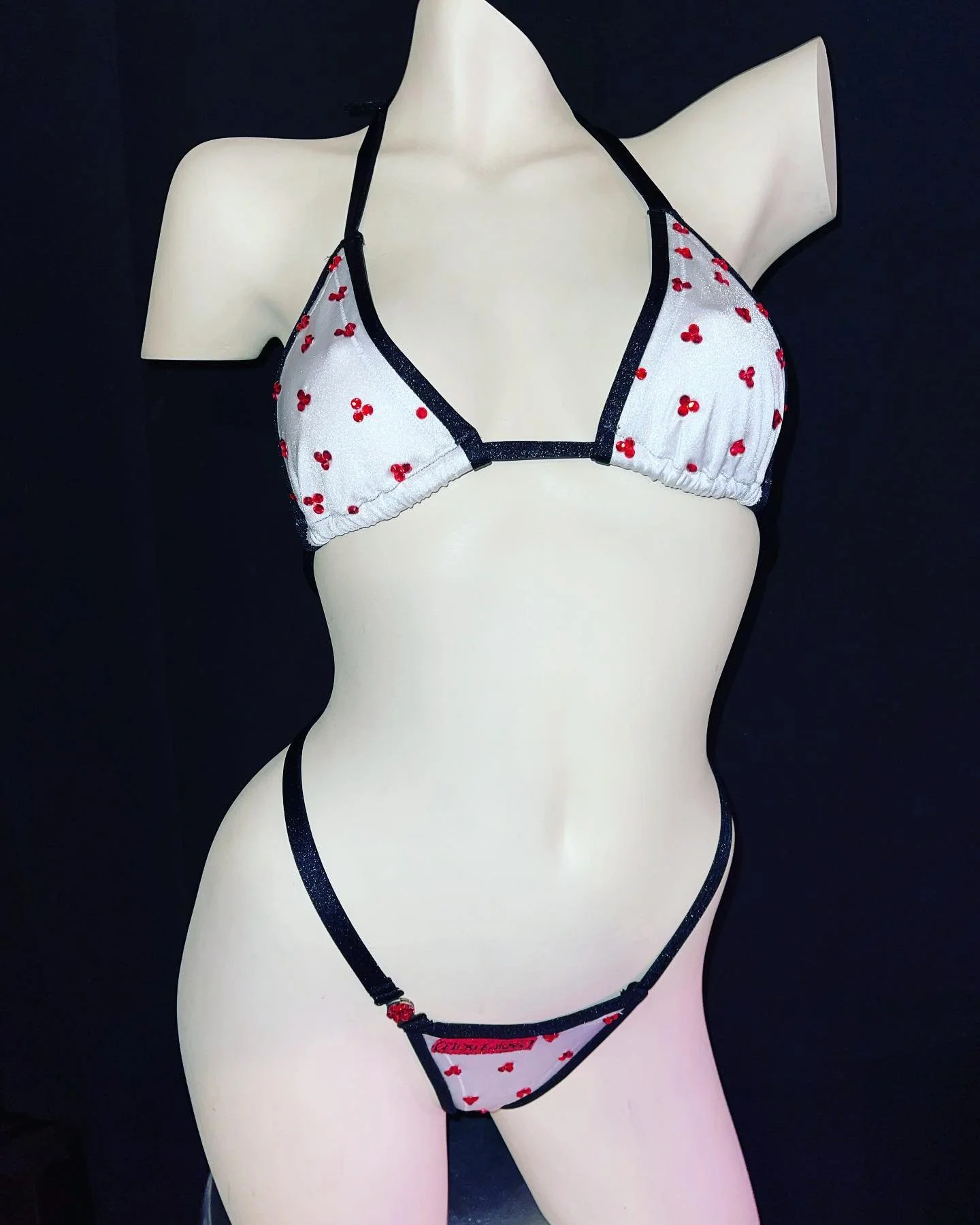 Mannequin wearing white bikini with cherry pattern and black trim.