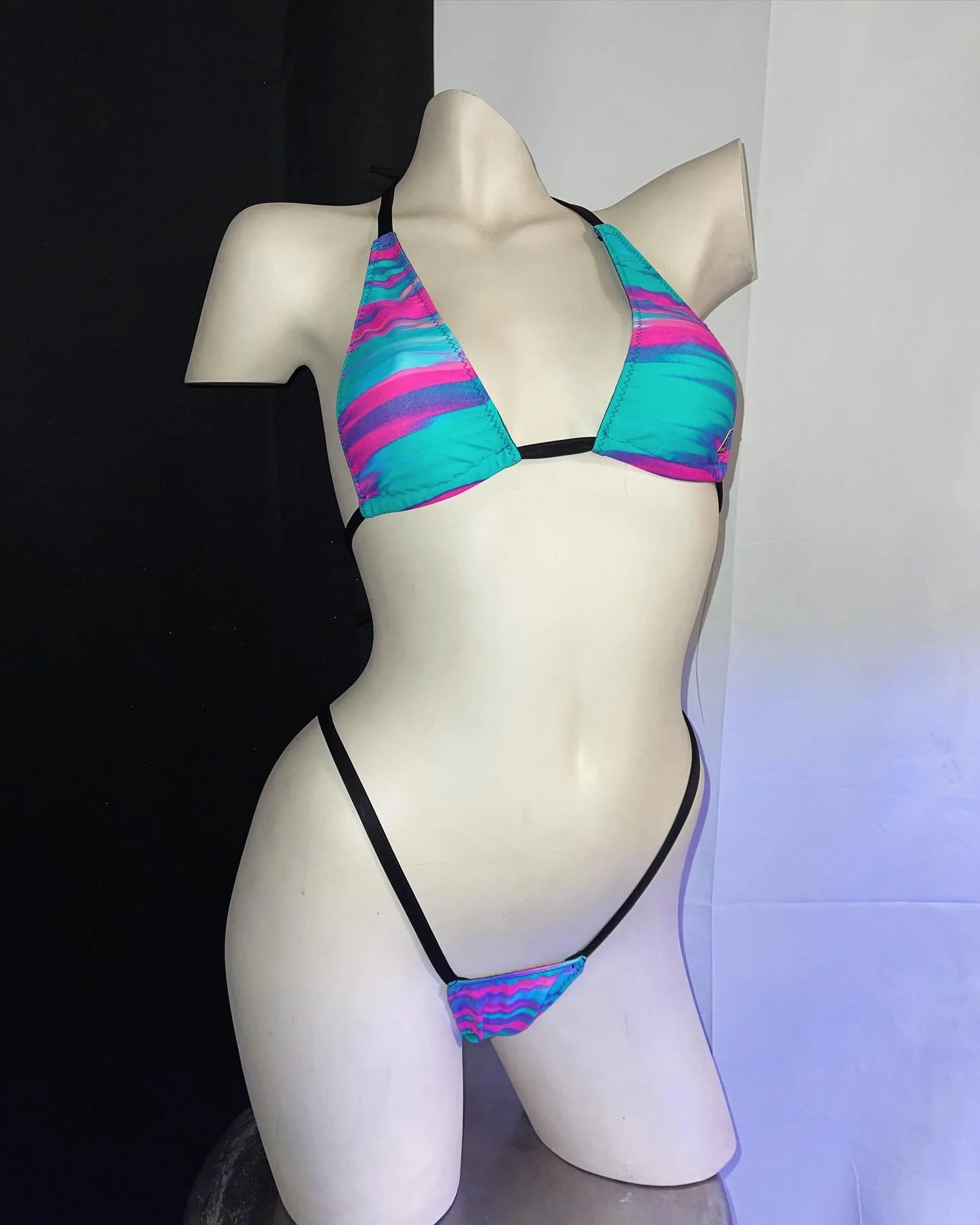 Mannequin in turquoise and pink striped bikini against a black and white background.