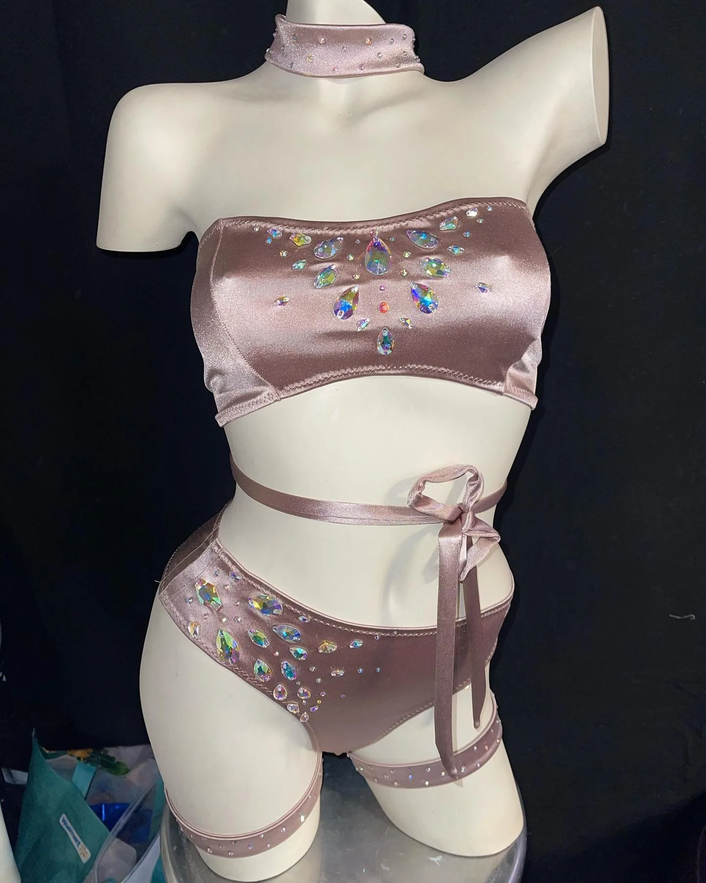 Mannequin wearing embellished satin lingerie set with choker, bandeau top, and high-waisted panties adorned with colorful gemstones and thin straps.