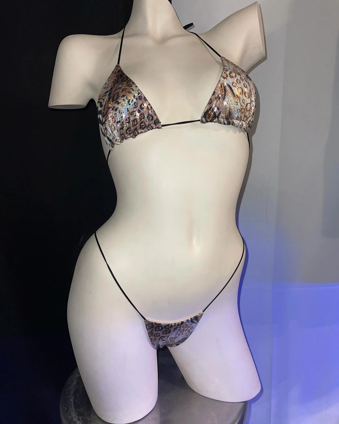 Mannequin wearing a leopard print bikini with a shiny finish on a dark background.