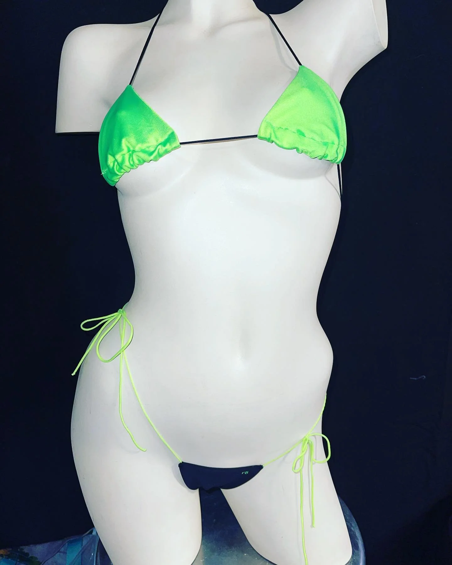 Mannequin wearing a neon green bikini against a black background.