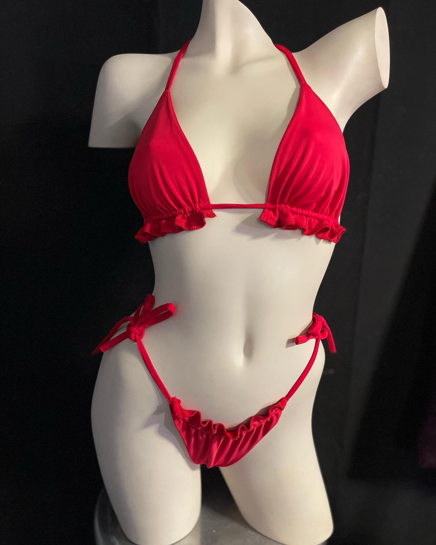 Mannequin wearing red bikini with ruffled edges on black background.