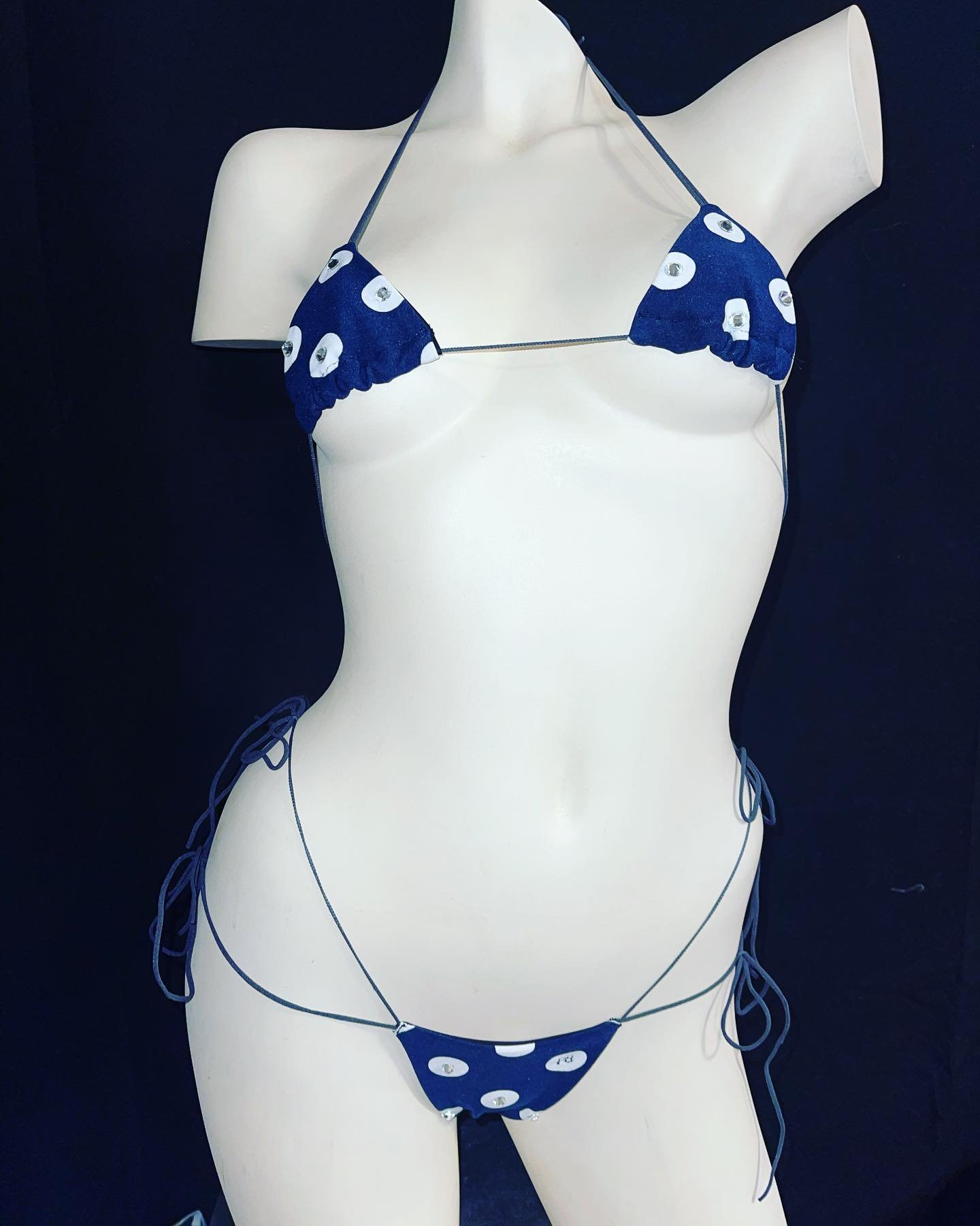 Navy blue bikini with white polka dots on a mannequin against a dark background.