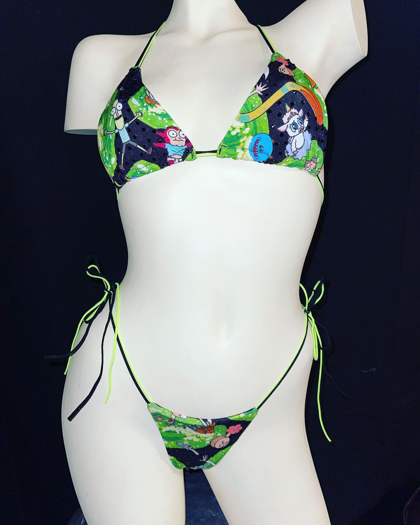 Mannequin wearing a green bikini with cartoon character print on a black background.