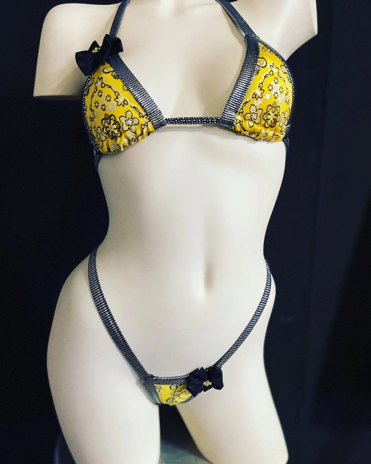 Mannequin wearing a yellow floral bikini with black bow accents and checkered straps.