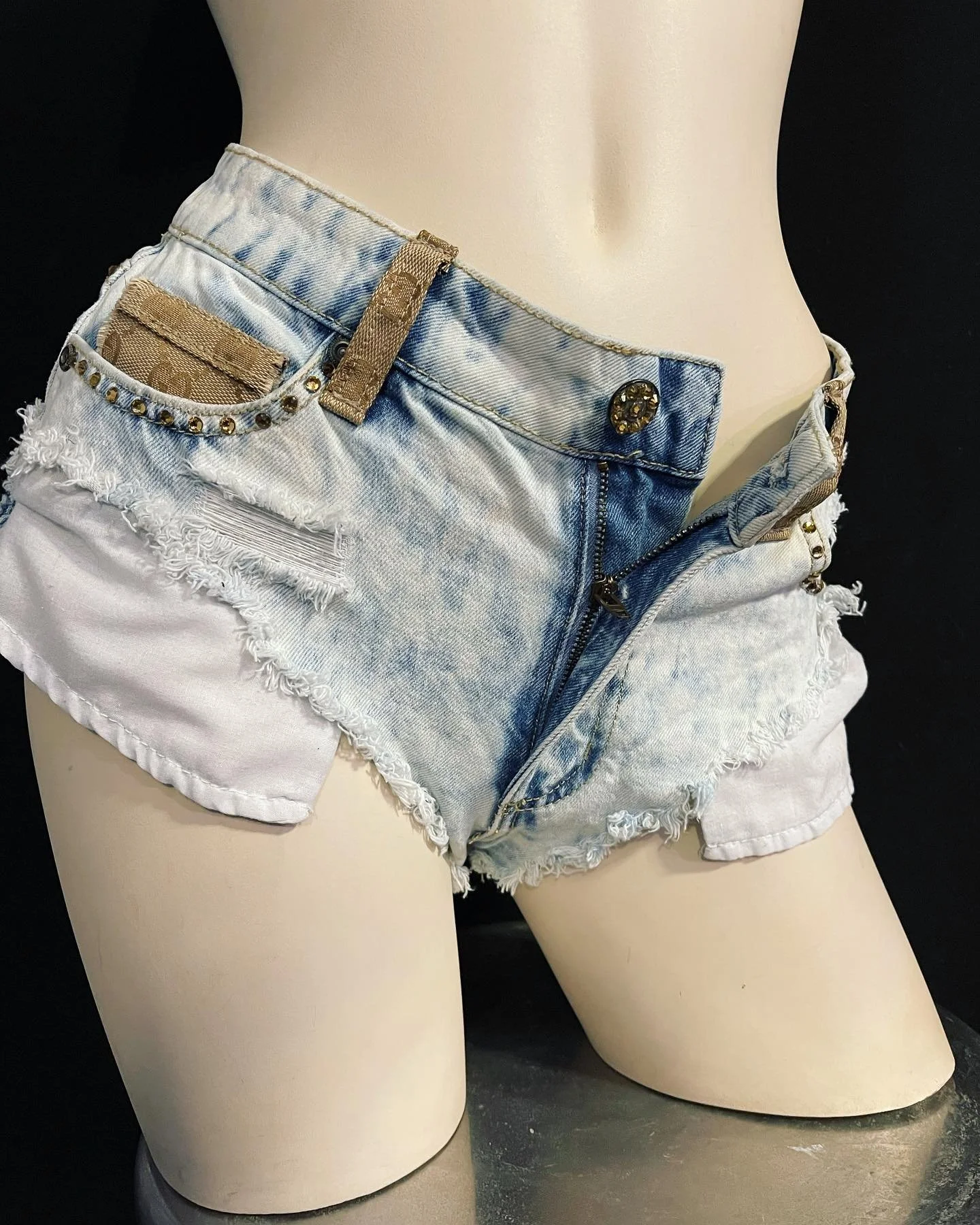 Low-rise, light-wash denim shorts with frayed edges on a mannequin.