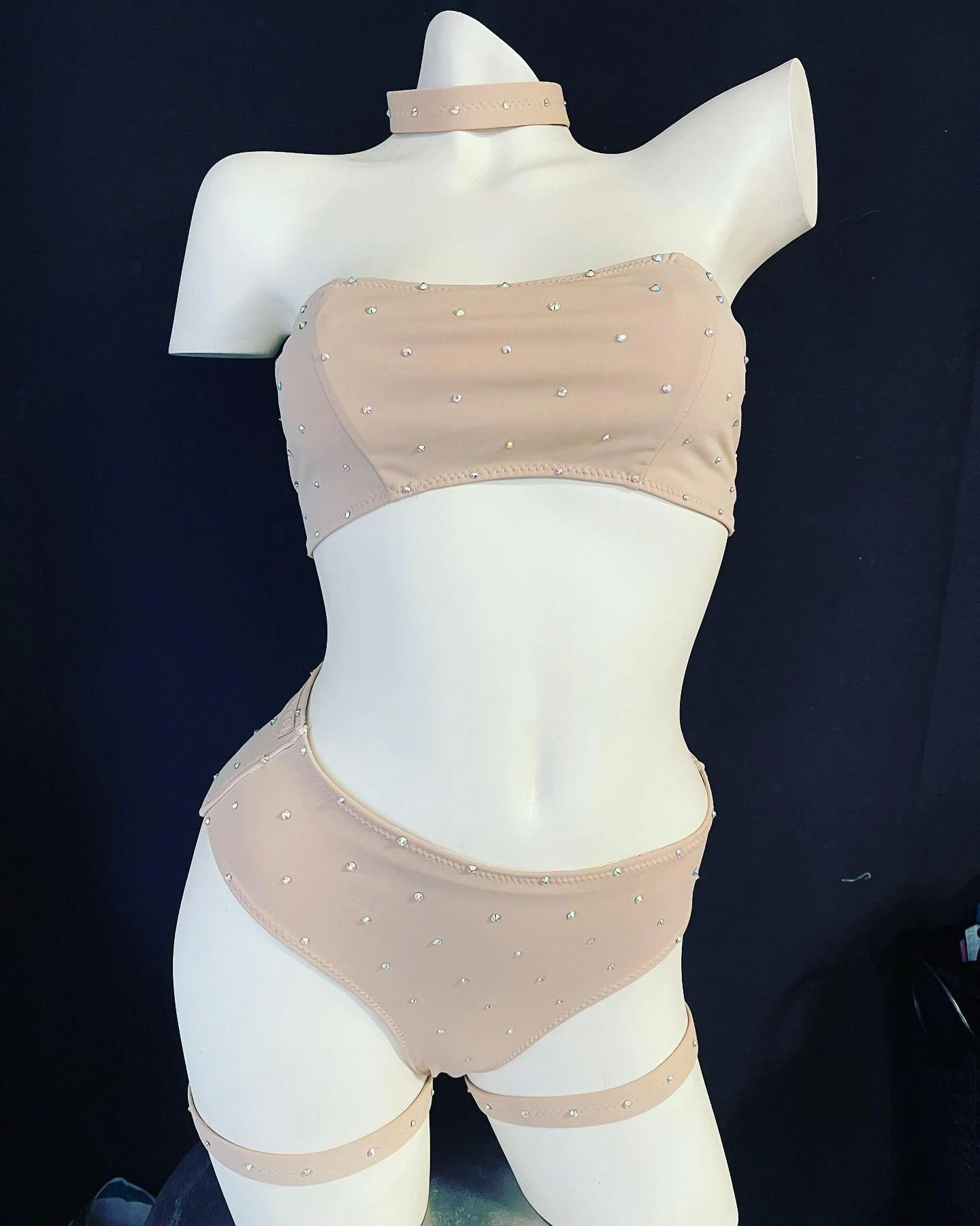 Mannequin wearing nude rhinestone-embellished lingerie set and choker on black background.