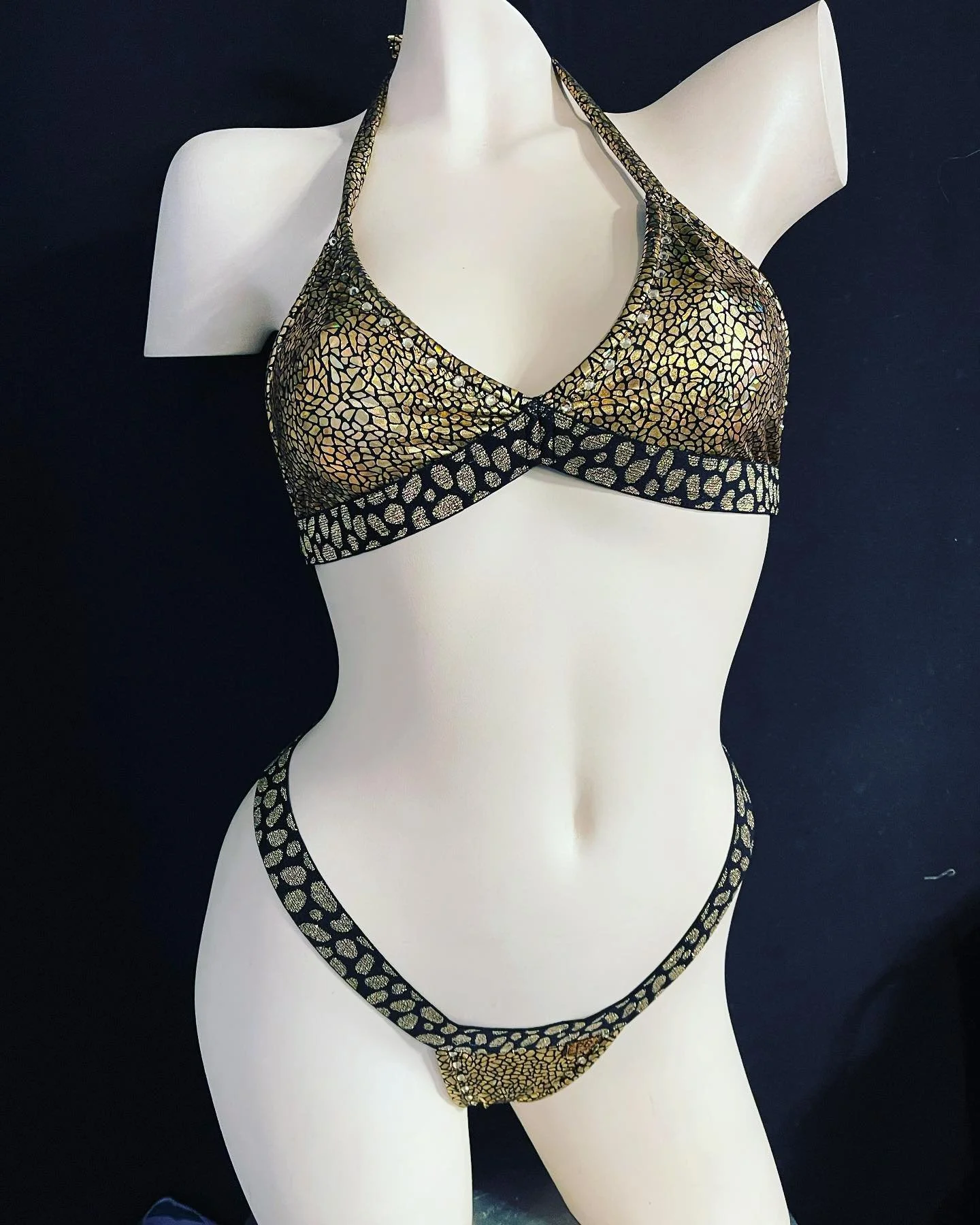 Mannequin displaying a gold and black bikini with a textured pattern against a dark background.